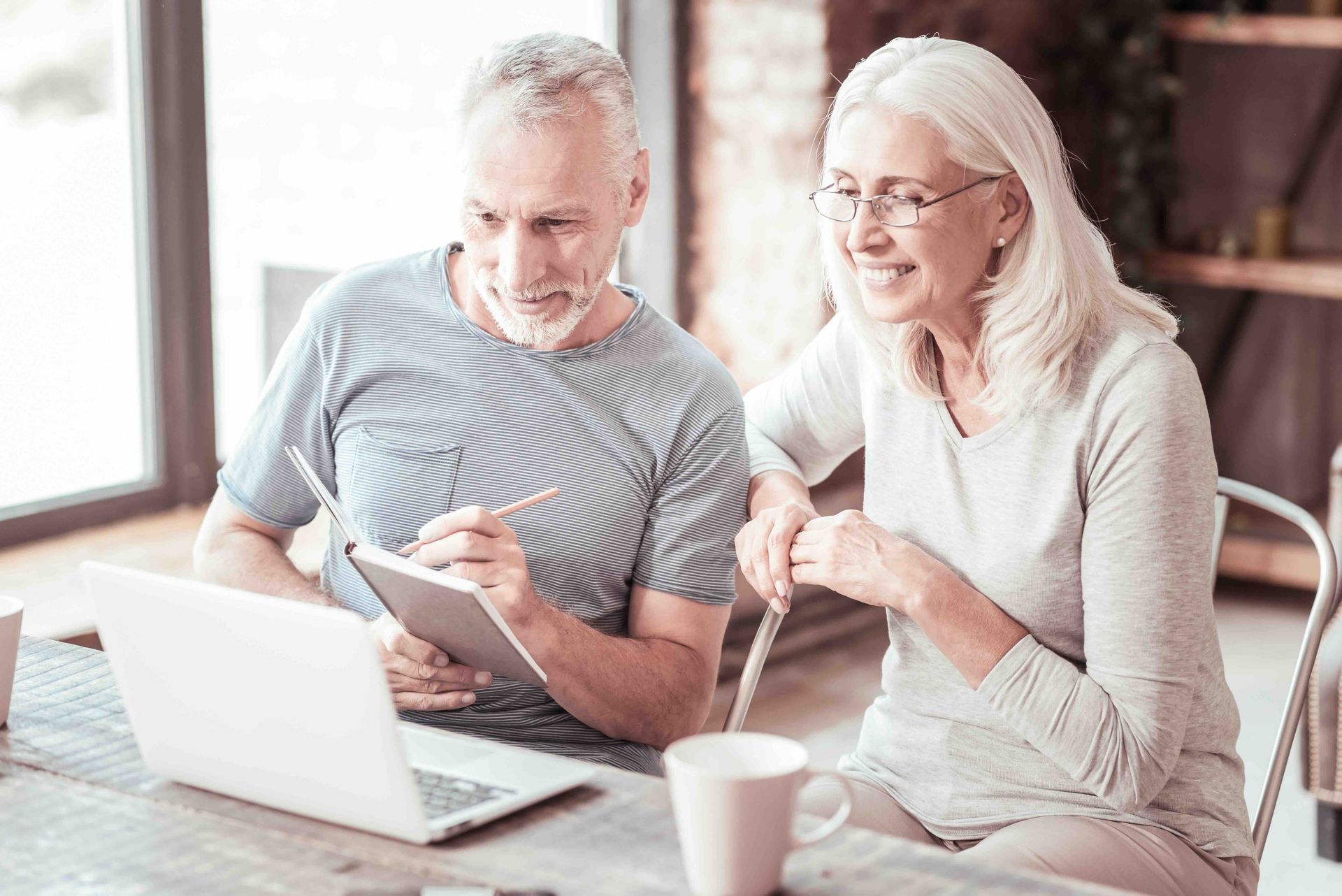 A man and a woman are sitting at a table looking at a laptop.