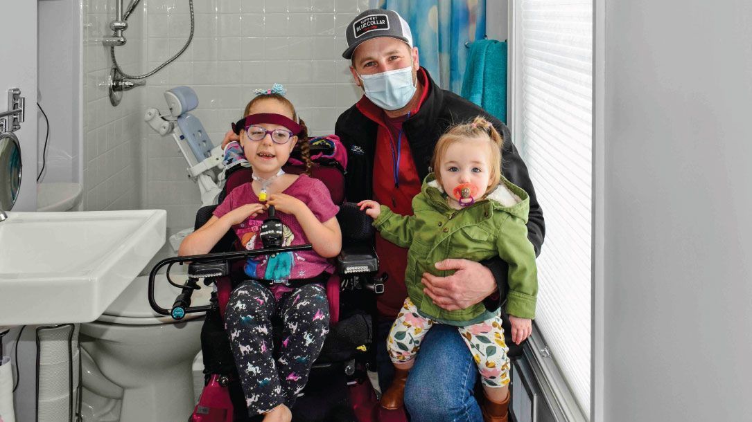 A man is holding two children in a bathroom. One of the children is in a wheelchair.