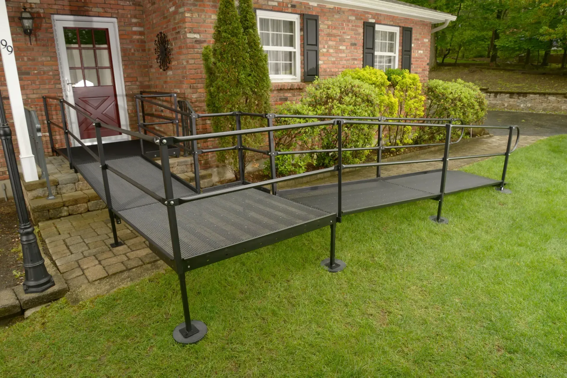 Black metal wheelchair ramp leading to a brick home's front door; set on grass.