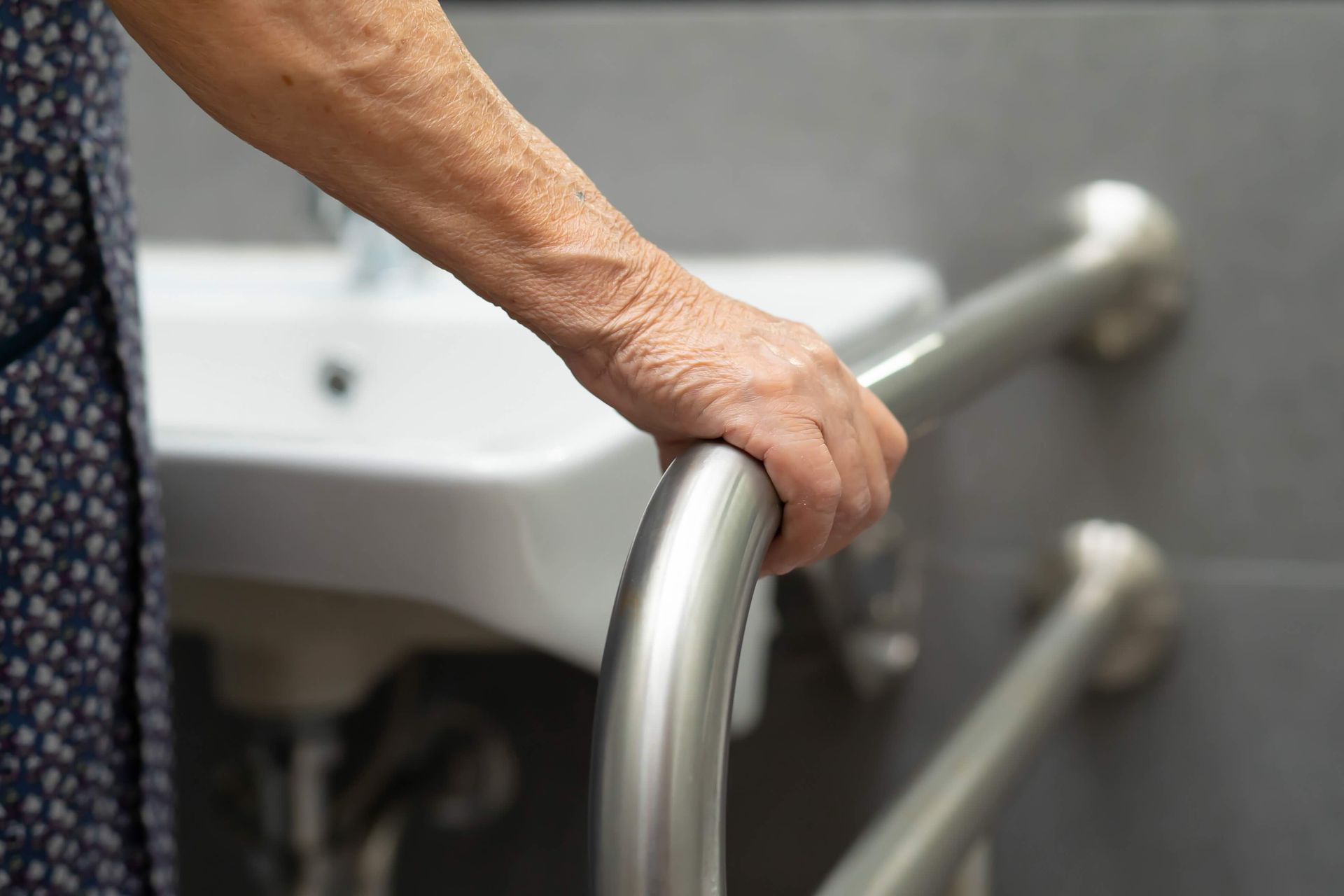 an elderly woman is holding onto a railing in a bathroom.