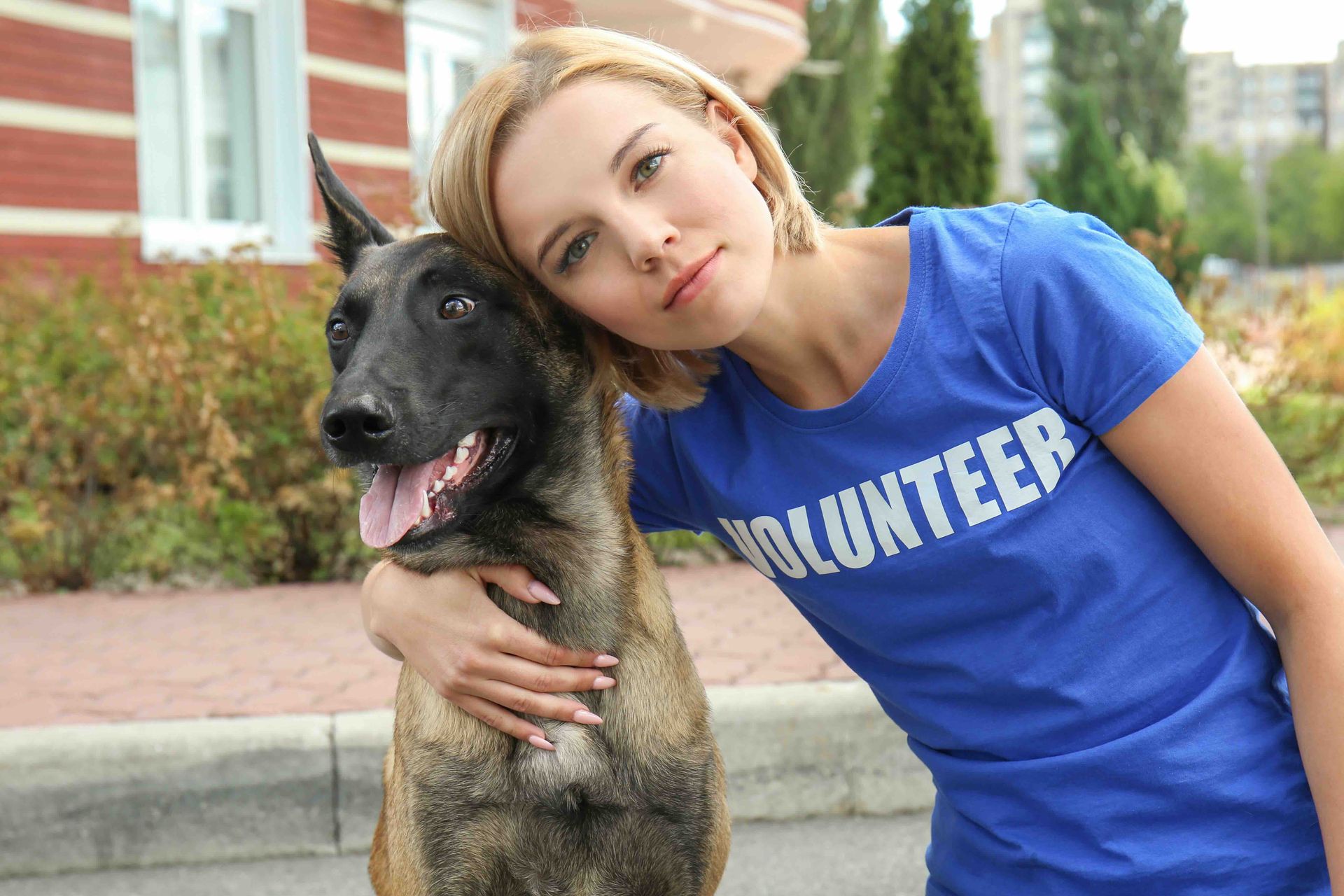 A woman in a blue volunteer shirt is hugging a dog.