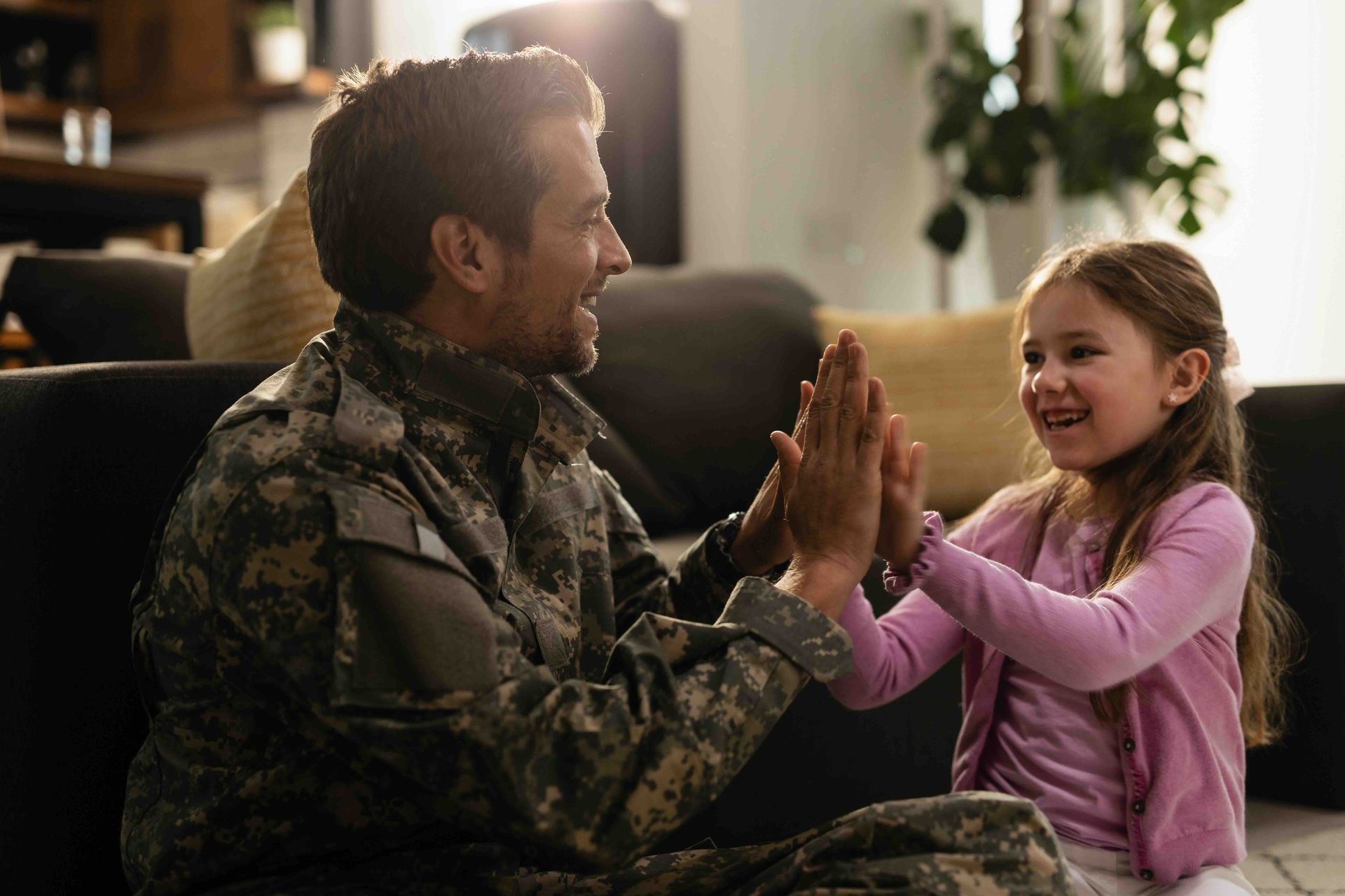 A man in a military uniform is giving a little girl a high five.
