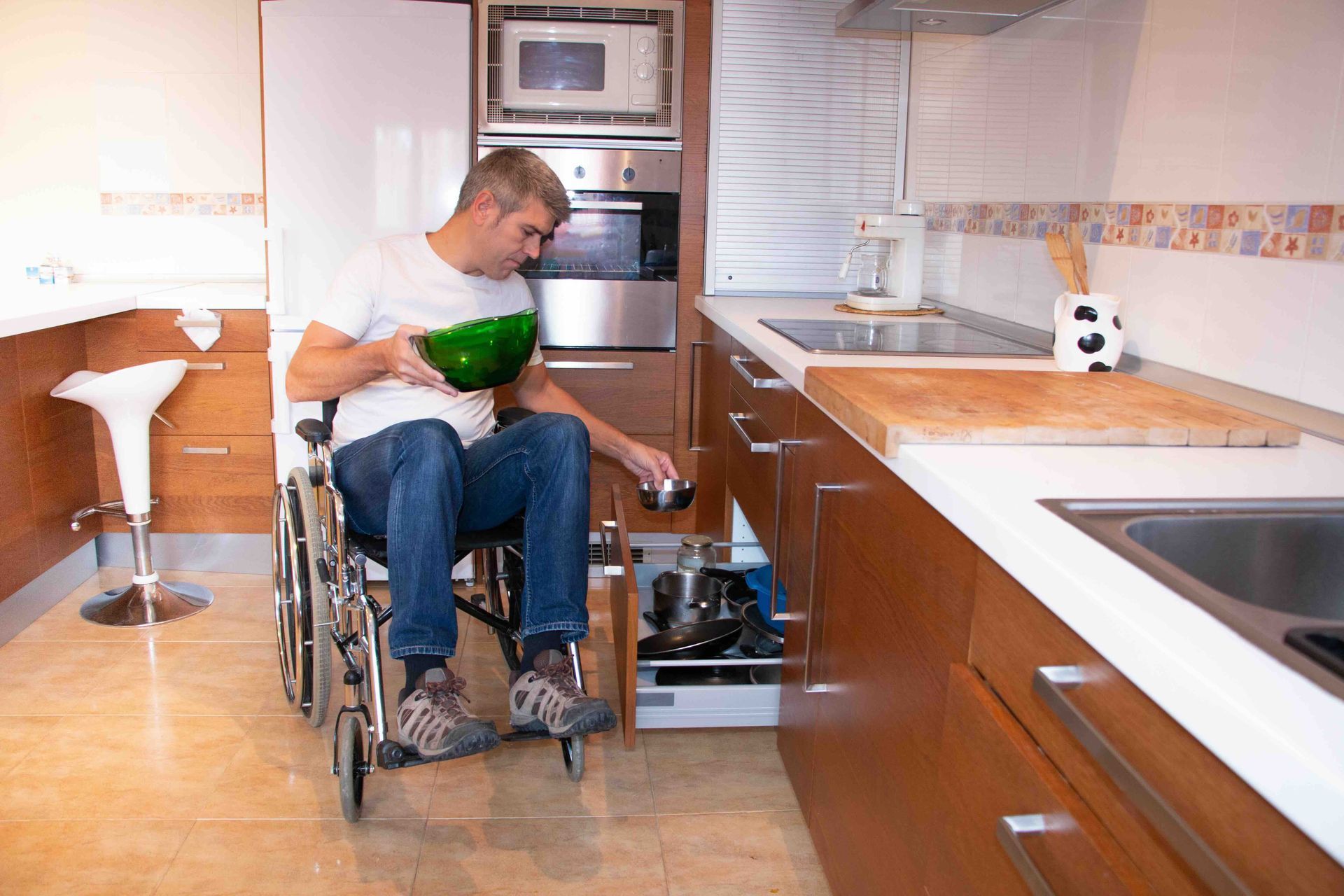 Man in wheelchair in kitchen, reaching for items in a lower cabinet.