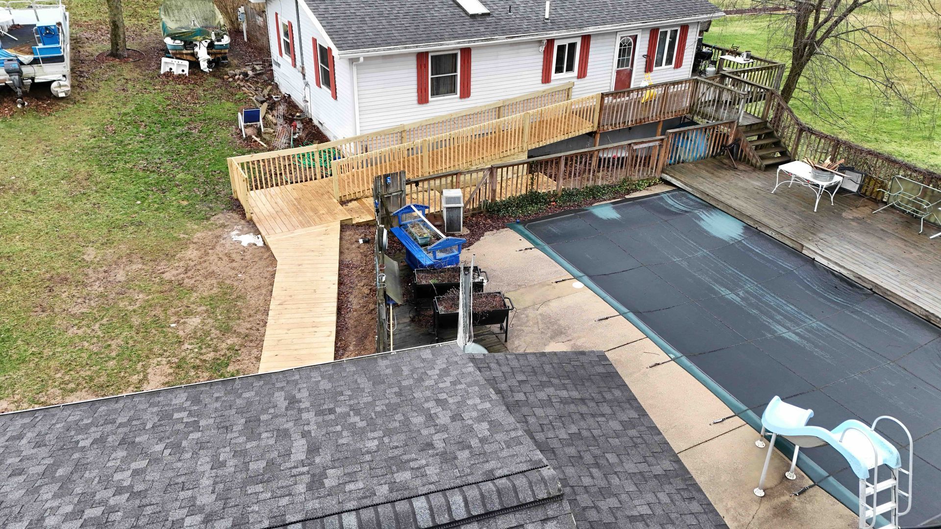 Aerial view of a house with a wooden ramp leading to the front door and a pool with a cover.