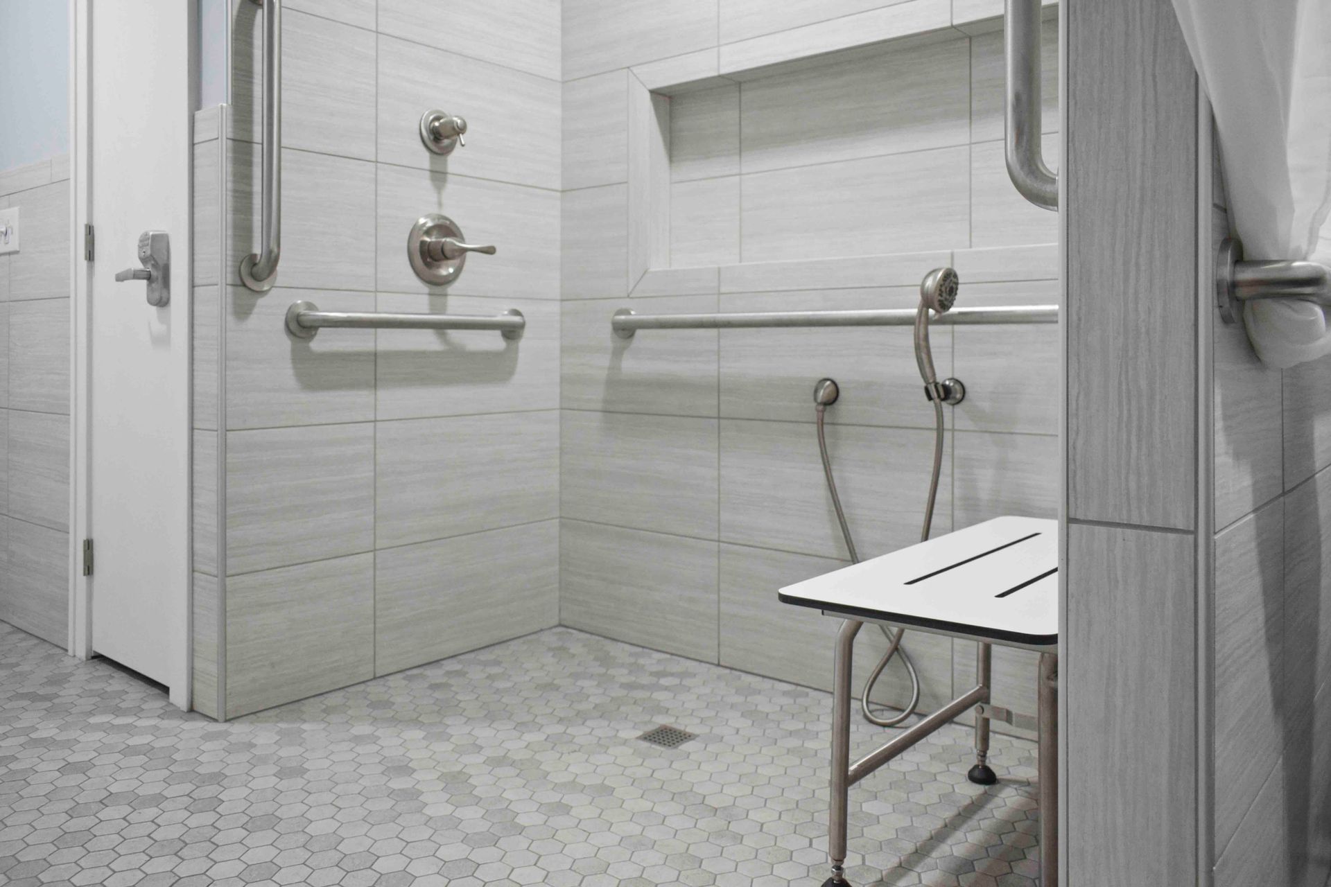 A wheelchair-accessible bathroom with a walk-in shower, grab bars, and a bench.