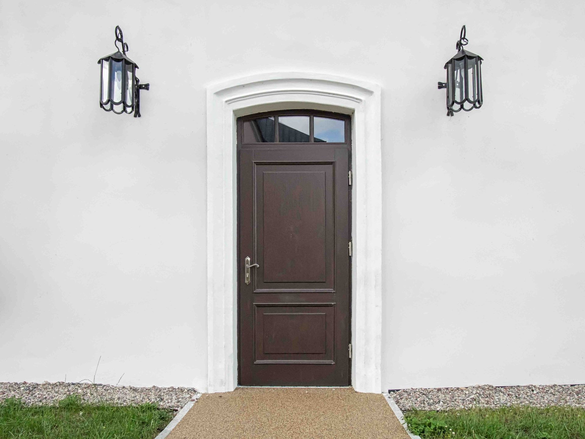 Brown door with white trim set in a white wall, flanked by black lanterns.