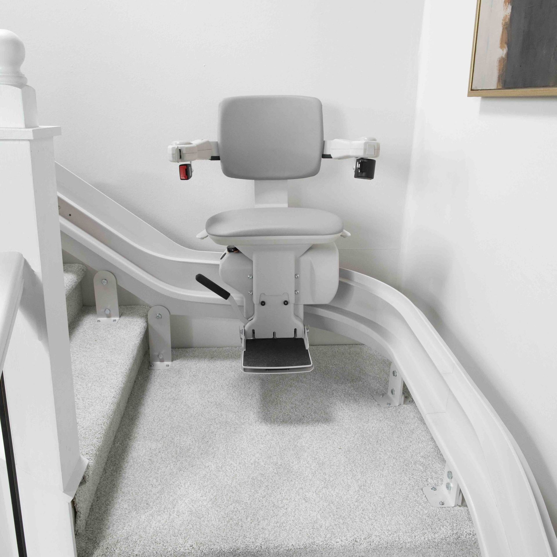 A white stair lift with a gray seat sits on the rails next to the stairs.