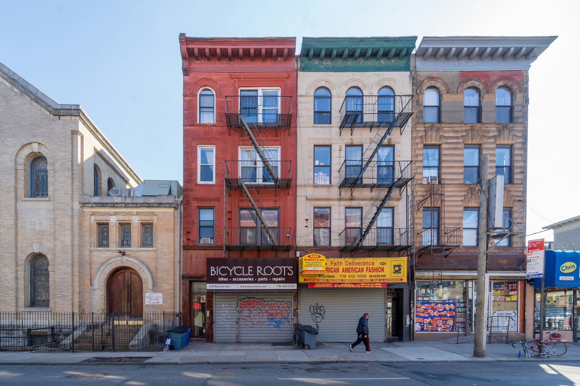 Row of colorful buildings with storefronts, fire escapes, and a person walking on the sidewalk.
