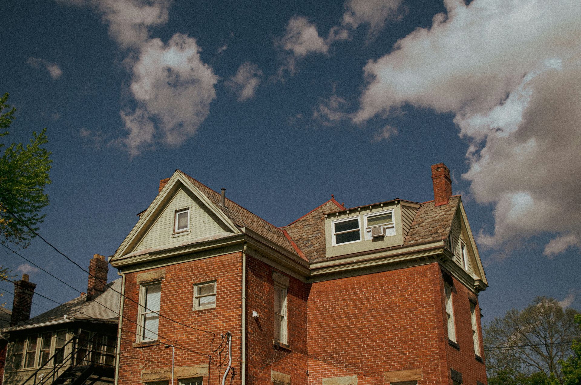 Red brick house with a gabled roof, under a blue sky with fluffy white clouds.