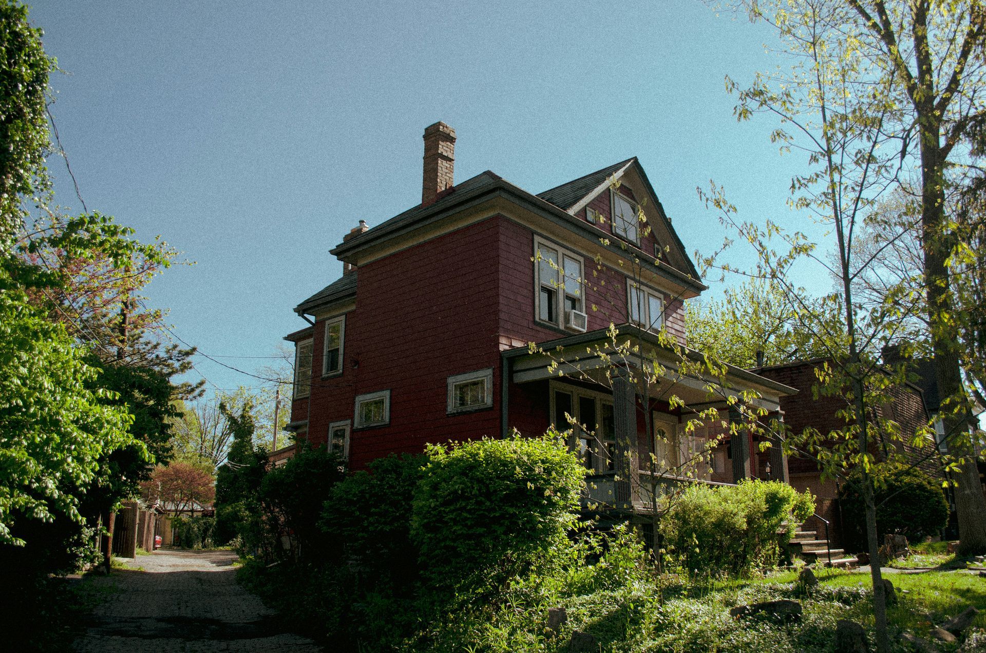 Red brick house with porch, trees, and blue sky.