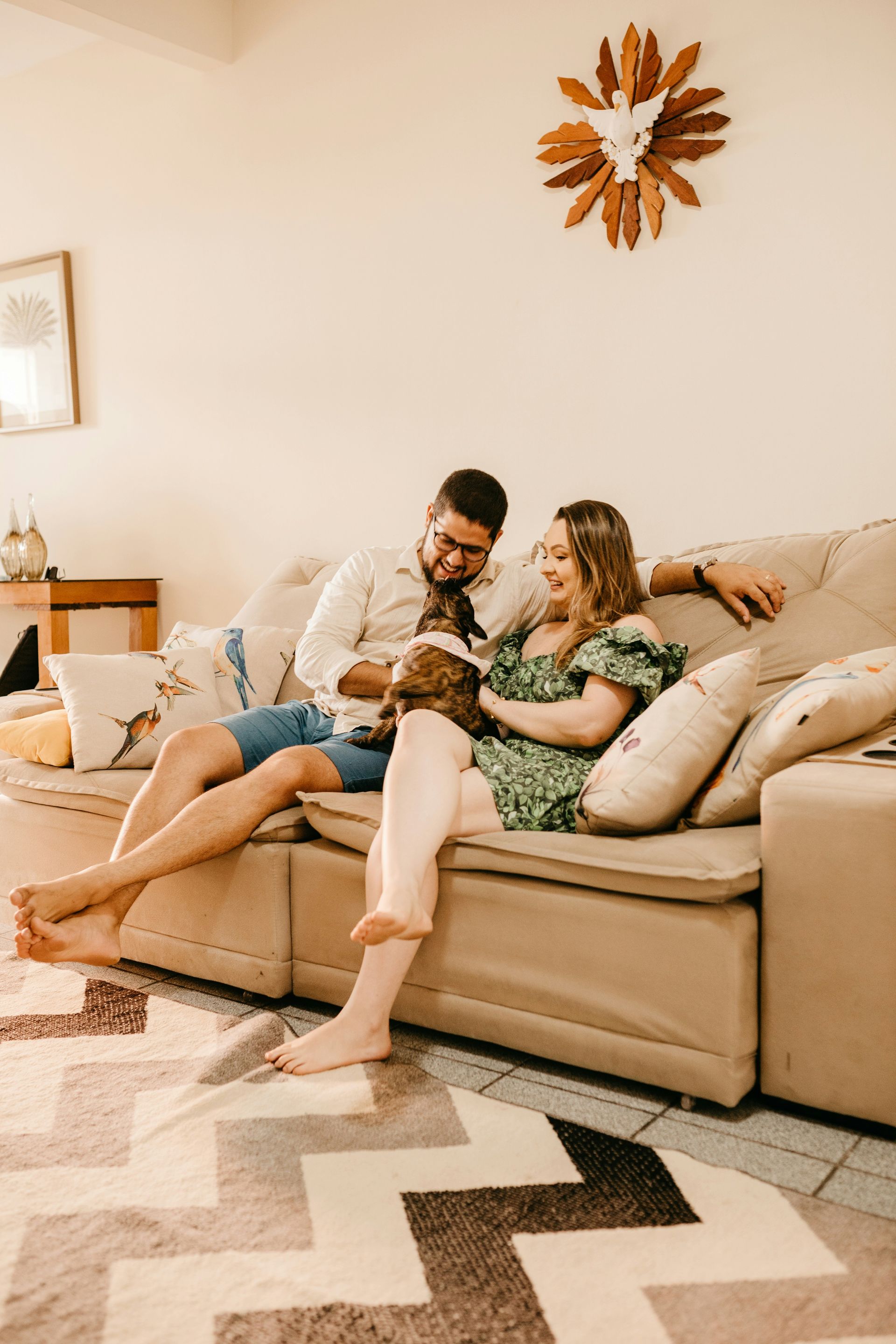 Couple on a sofa petting a small dog. Light-filled living room.