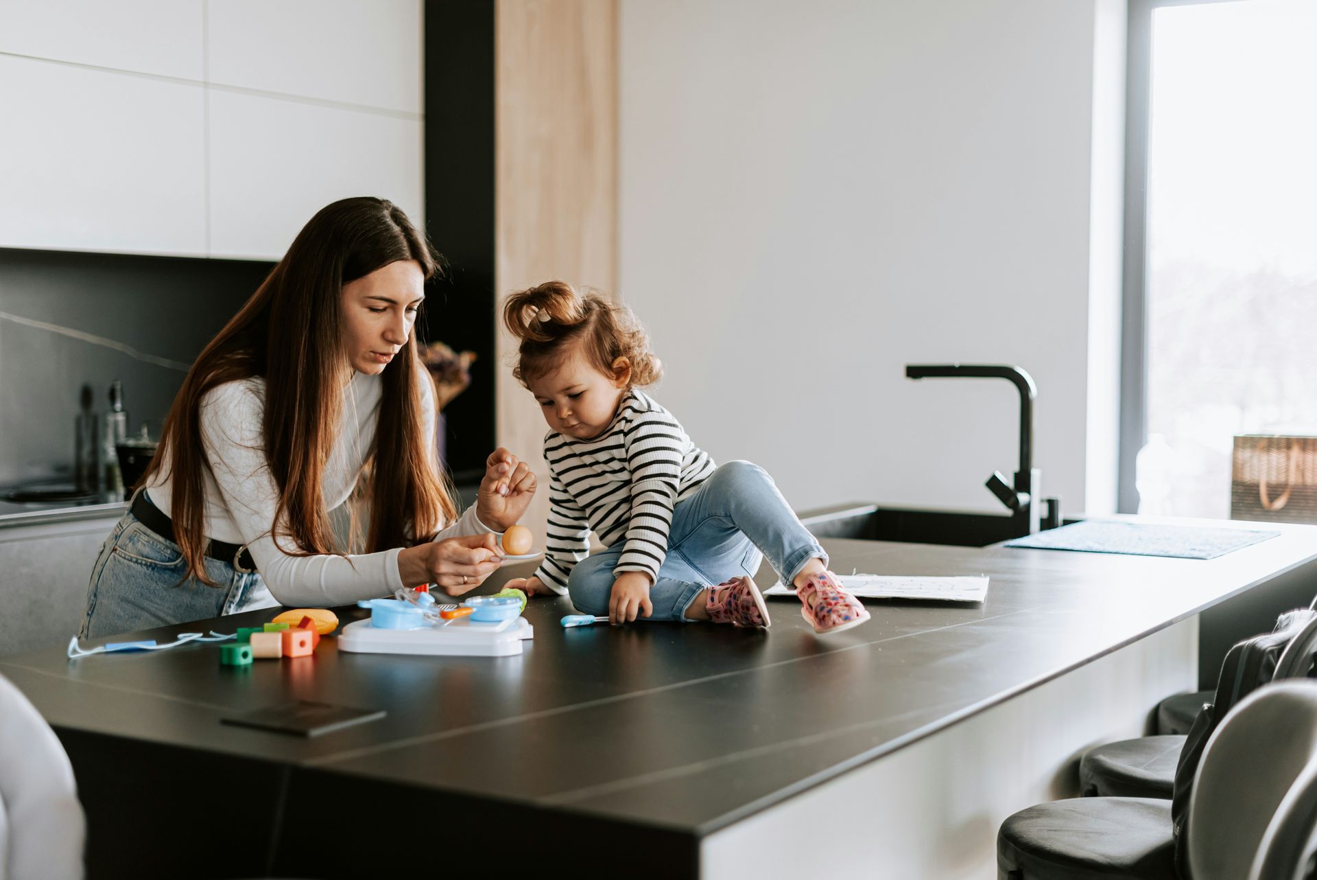 Woman and child playing with toys on a kitchen counter.