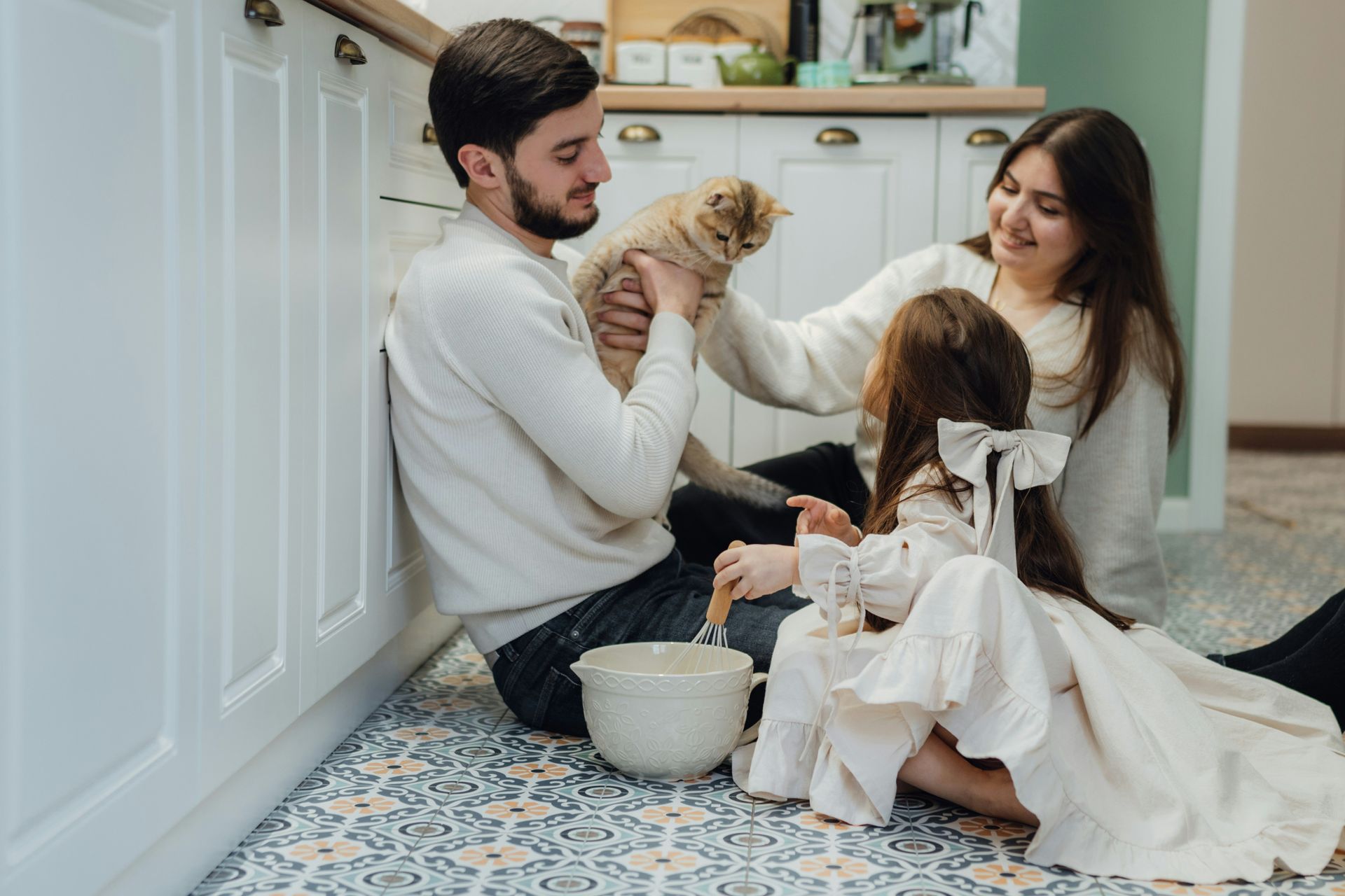 Family in kitchen, petting a cat, daughter holding bowl, smiling.