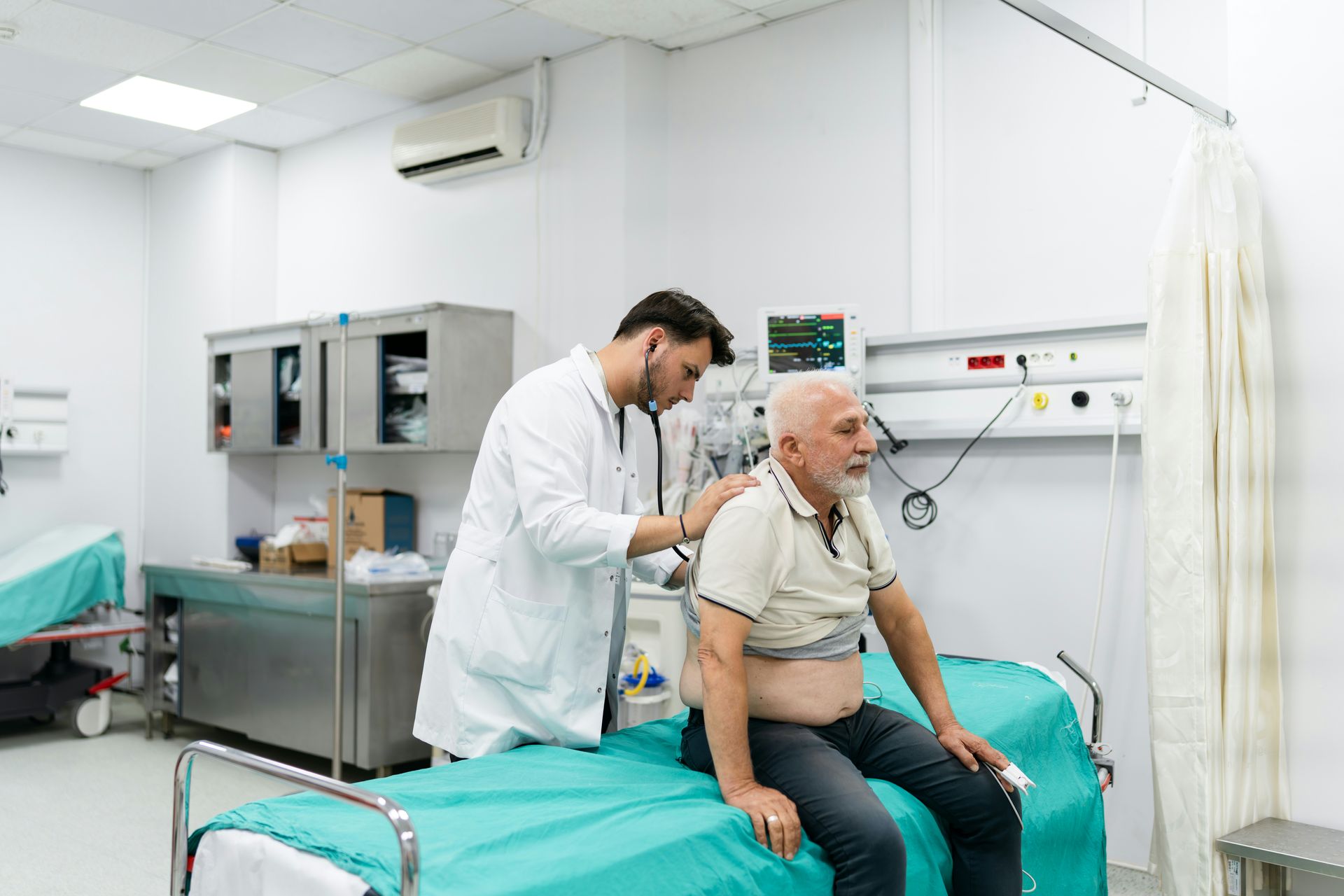 Doctor examining a patient's back with a stethoscope in a hospital room.