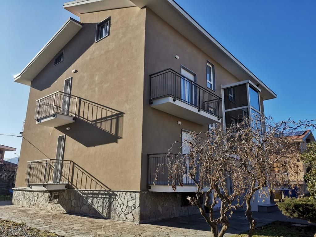 Casa marrone a due piani con balconi, base in pietra e albero spoglio sotto un cielo limpido.