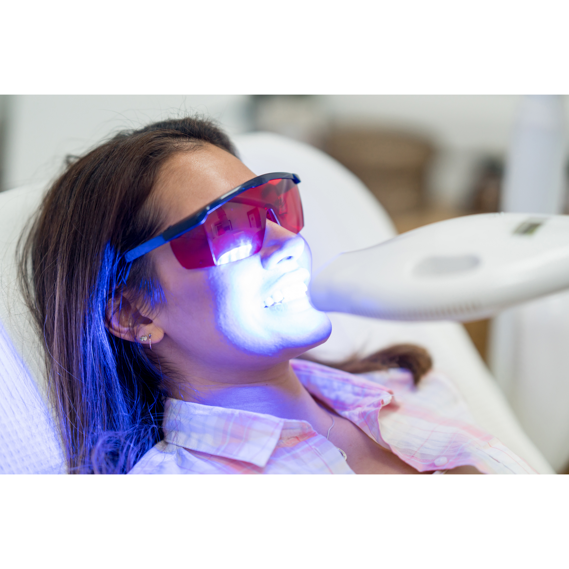 A woman is getting a teeth whitening treatment at a dental office.