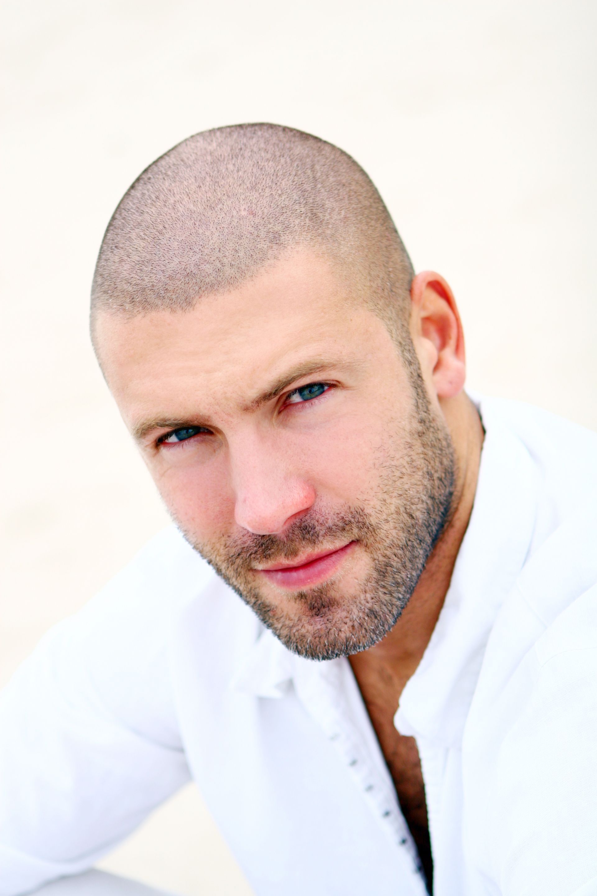 A shirtless man with a beard is smiling and touching his hair.