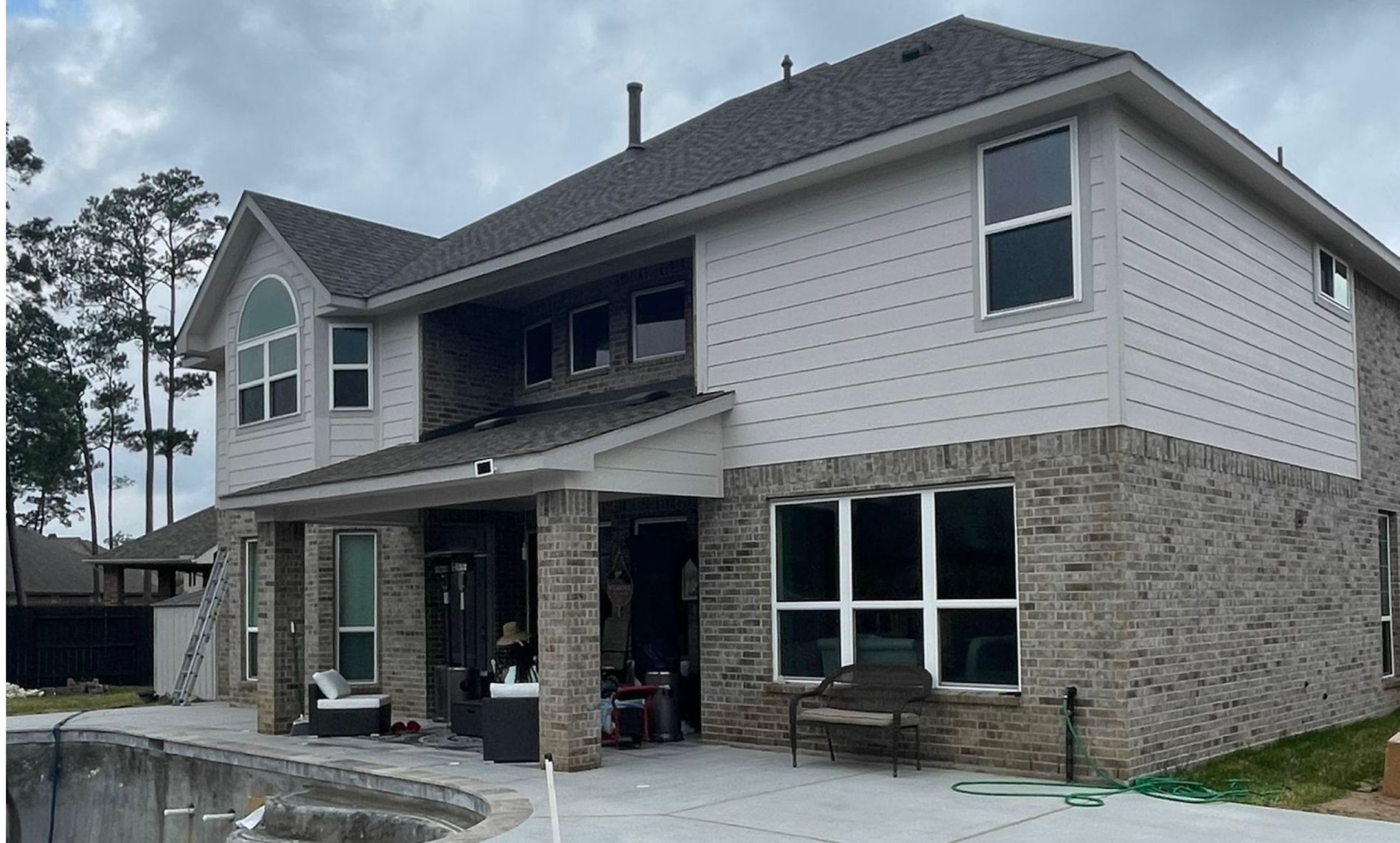 Two-story house with gray brick and siding, windows, and a covered patio. Cloudy sky in the background.