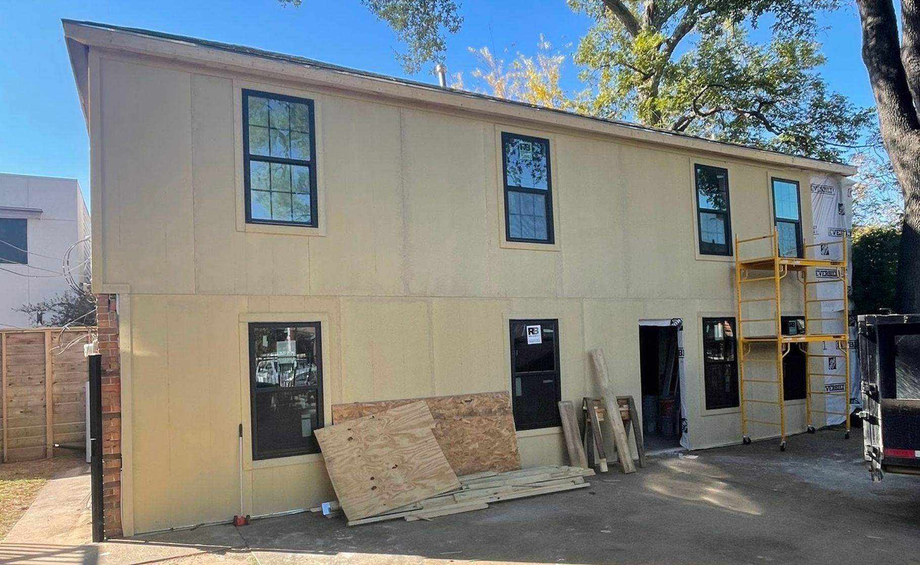 Two-story building under construction; tan siding, black-framed windows, and construction materials visible.