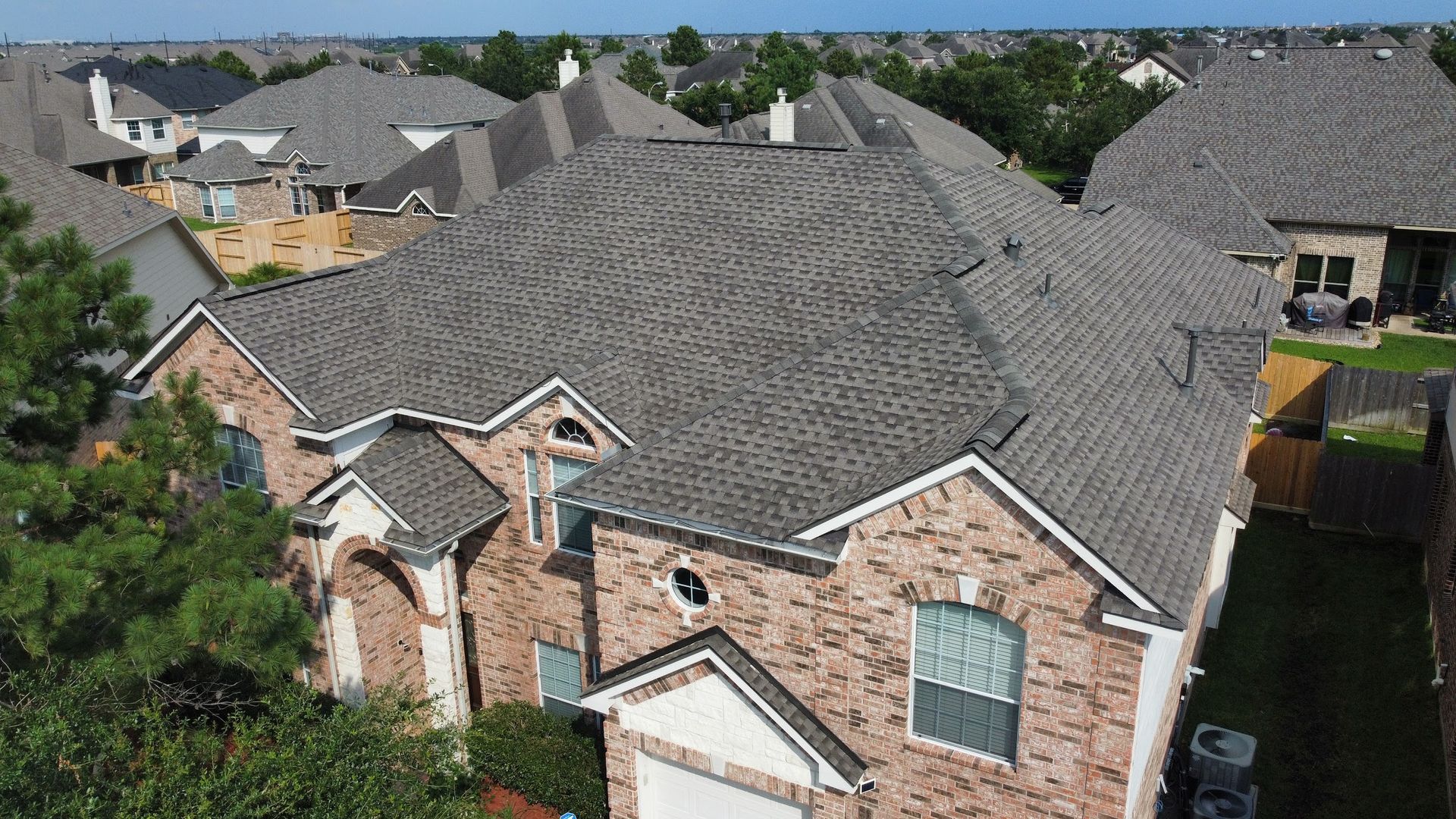 Aerial view of a brick house with a gray shingle roof in a suburban neighborhood.