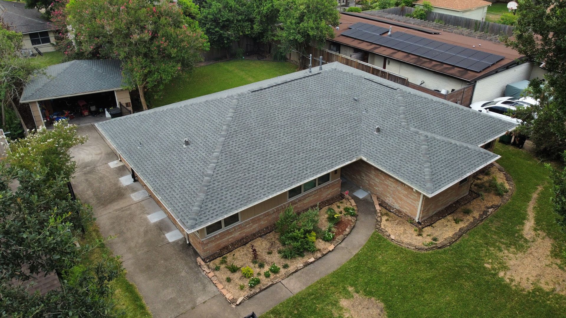 Aerial view of a single-story brick house with a gray roof, a driveway, and a green lawn.