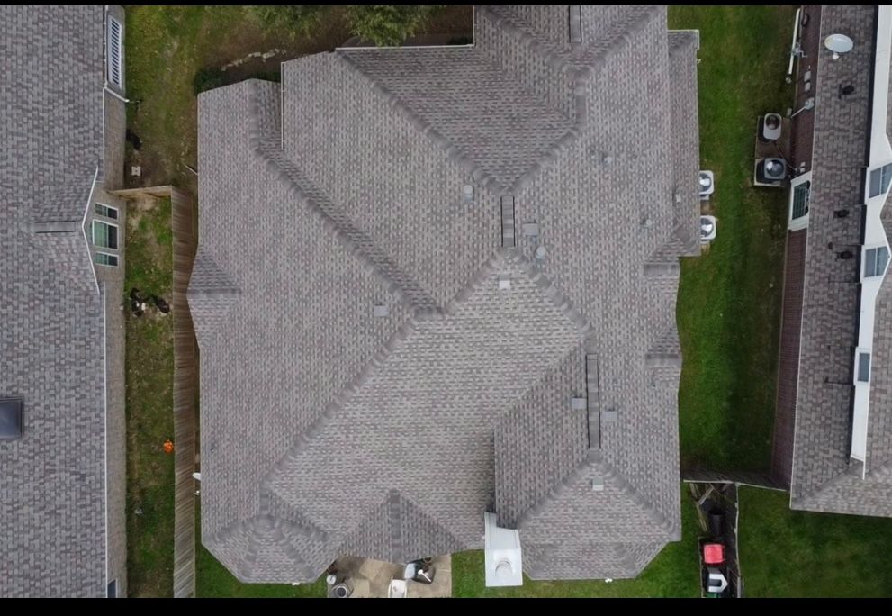 Overhead view of a house with a gray roof surrounded by green grass and neighboring houses.