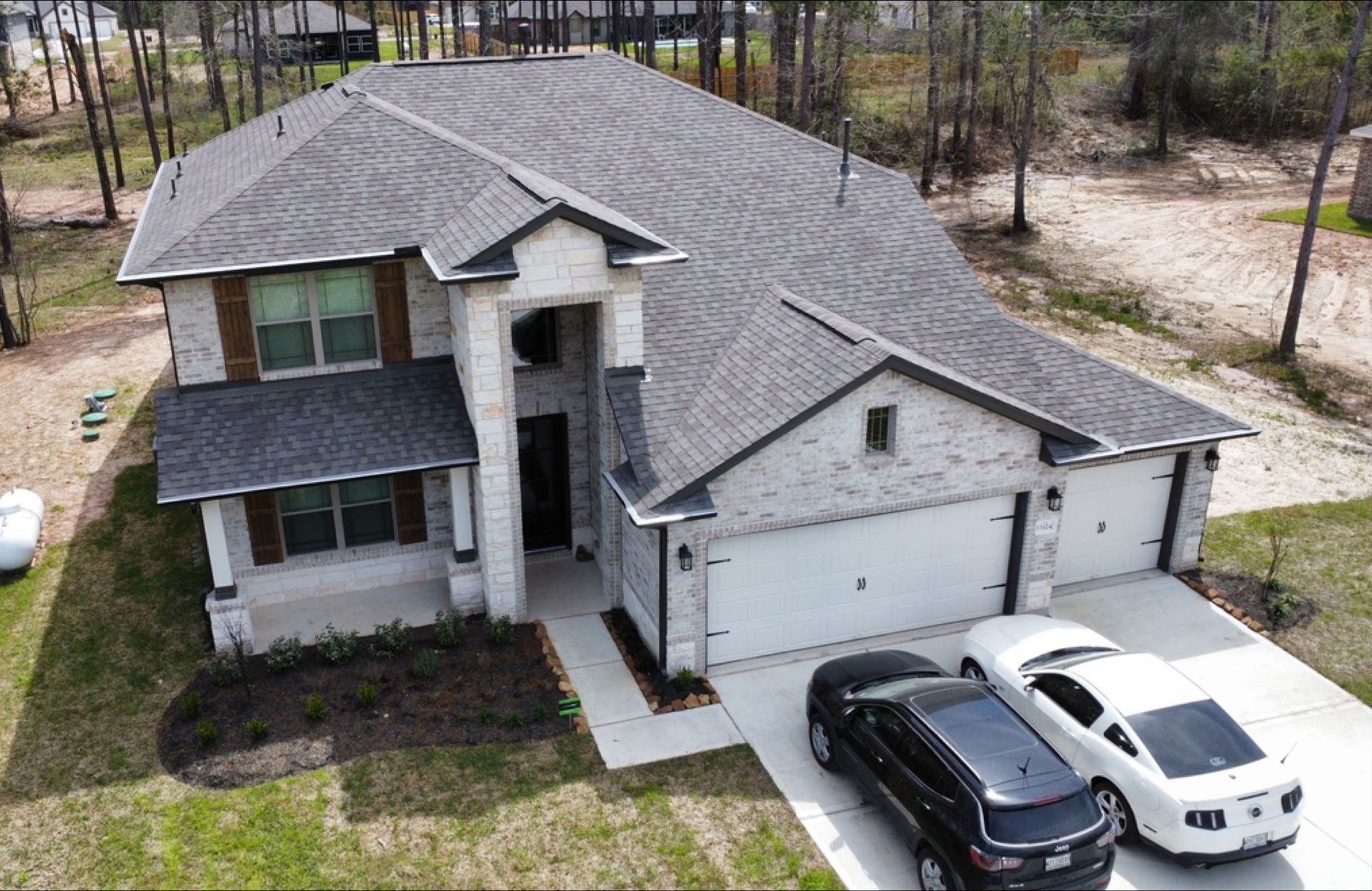 Two-story house with gray shingle roof and light brick facade. Two cars parked in the driveway.