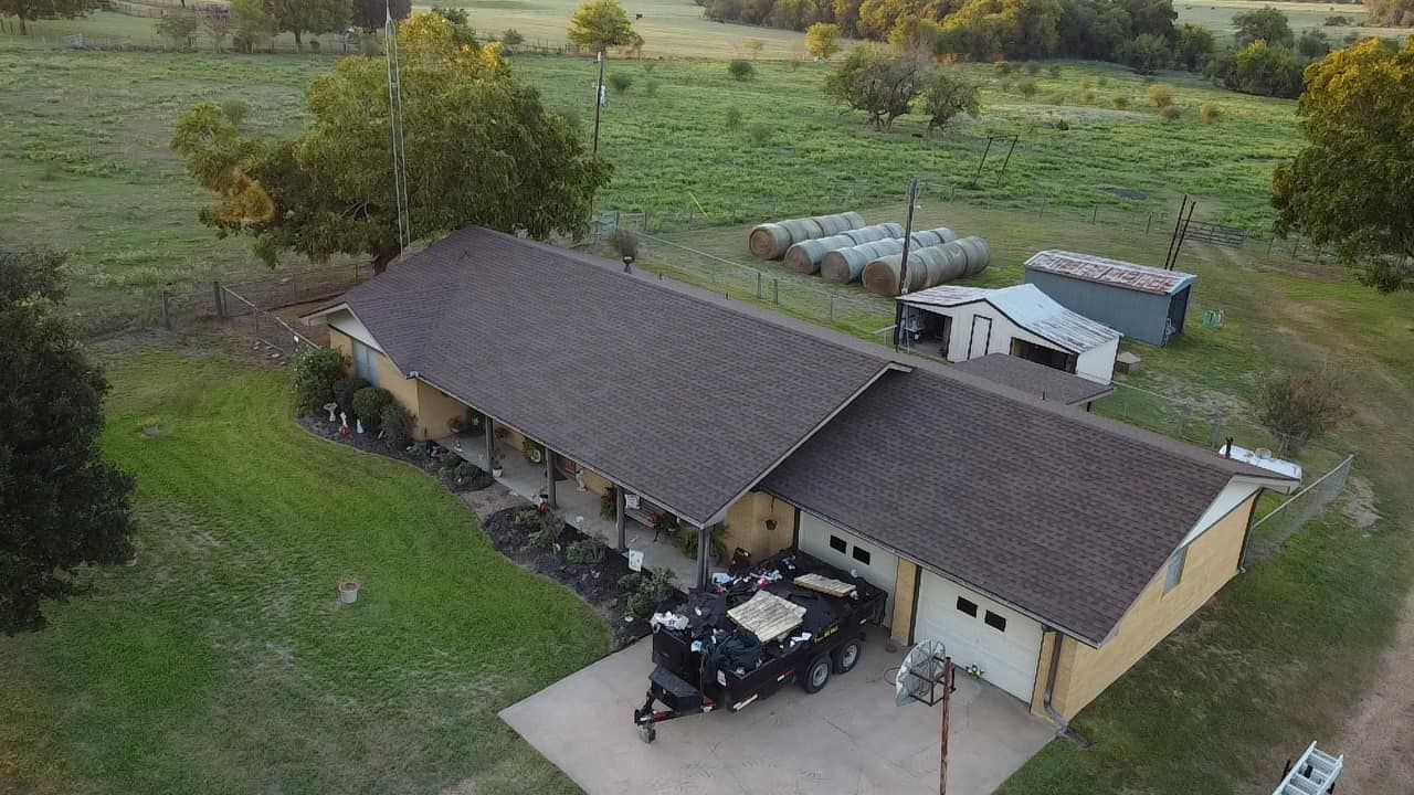 Aerial view of a ranch-style house with a brown roof and a trailer parked in front.