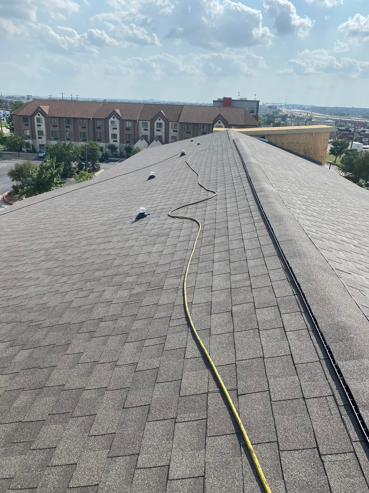 View from a rooftop, with shingles and a yellow cable. In the background is a building with a red roof and a blue sky.