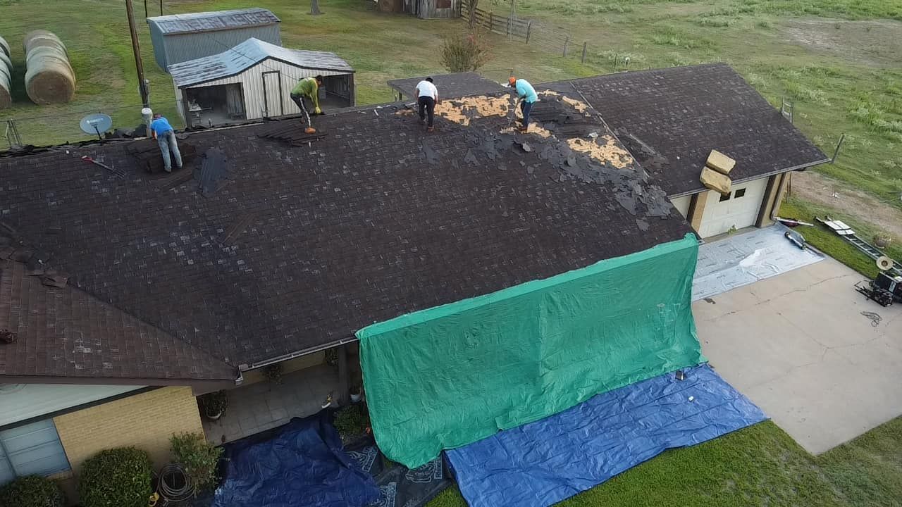 Roofers repairing a house roof with some areas covered in green and blue tarps.