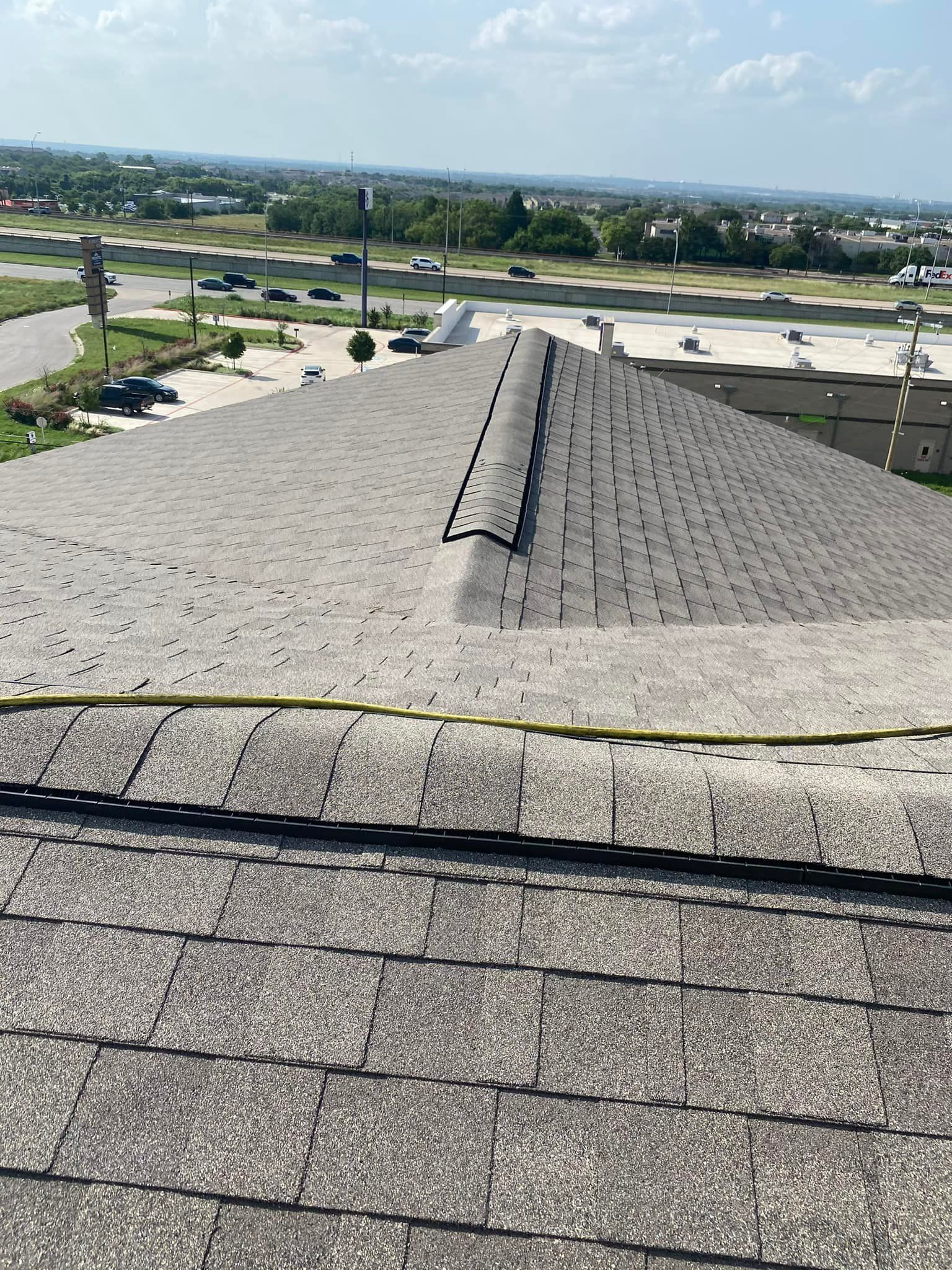 View from a rooftop of weathered, gray shingles; a yellow rope lies across them.  Distant urban landscape is visible.