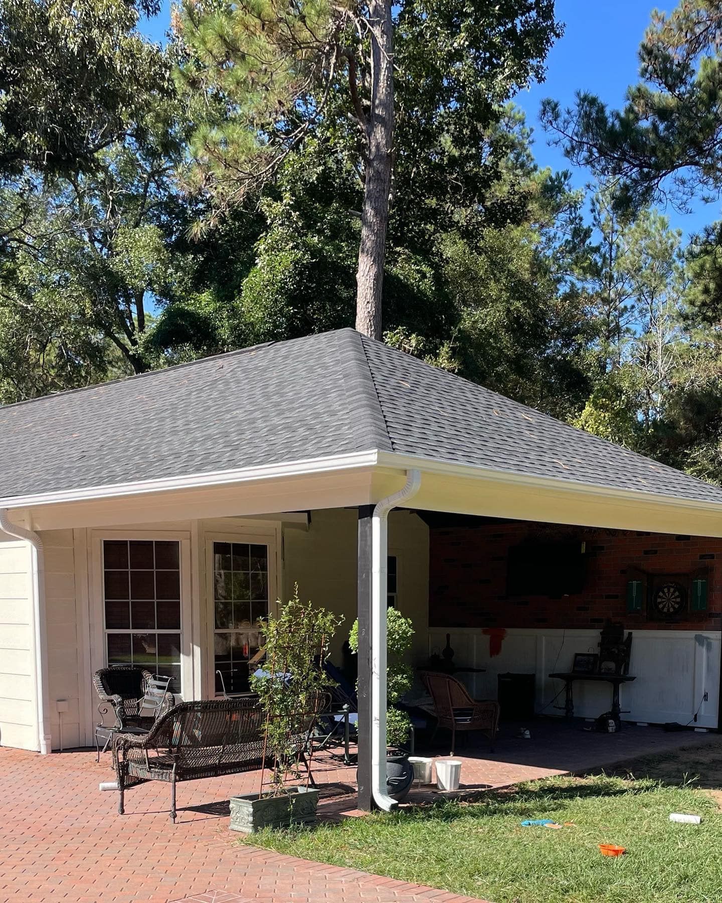 Outdoor patio with a covered roof, brick floor, seating, and a tree growing through the roof.