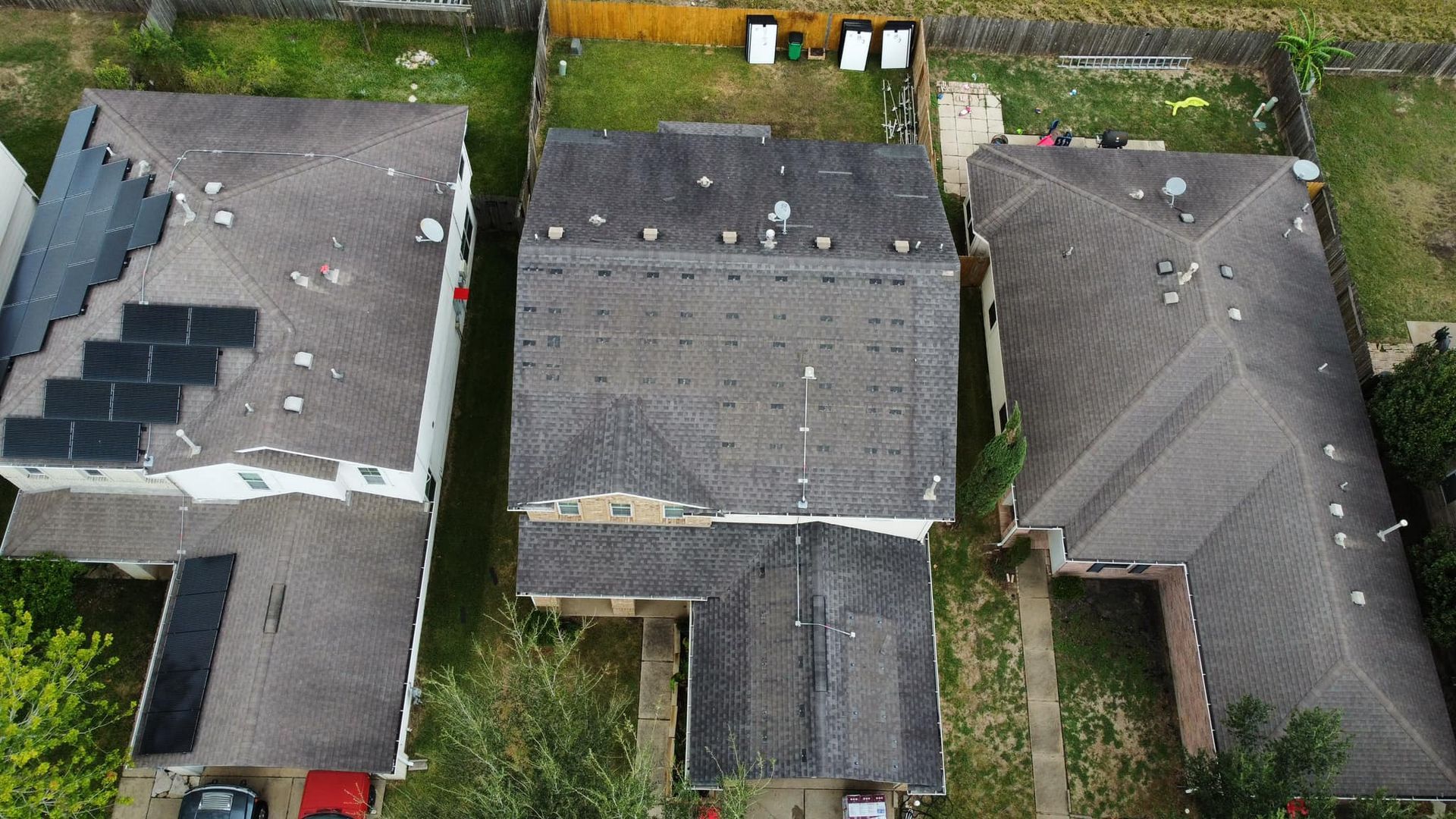 Overhead view of three houses with damaged roofs, likely in a residential neighborhood.