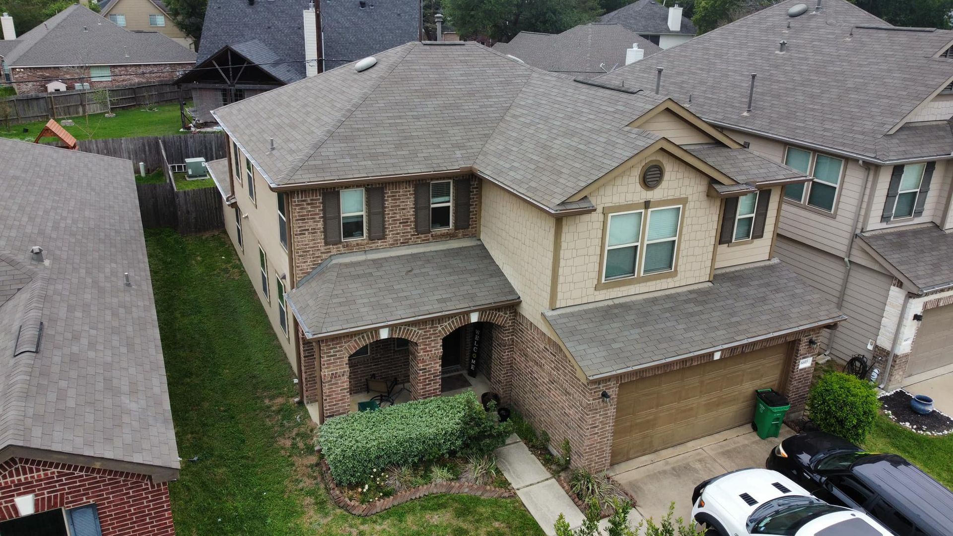 An aerial view of a two-story house with a brown roof and brick and beige exterior.
