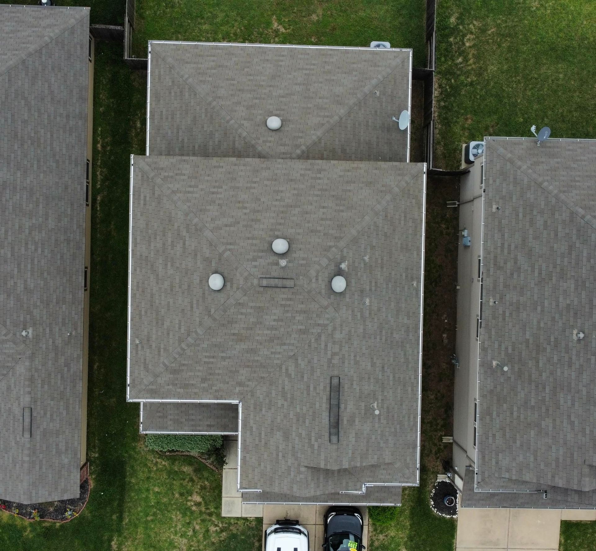 Overhead view of a house with a gray roof, located between two similar houses with surrounding green lawns.