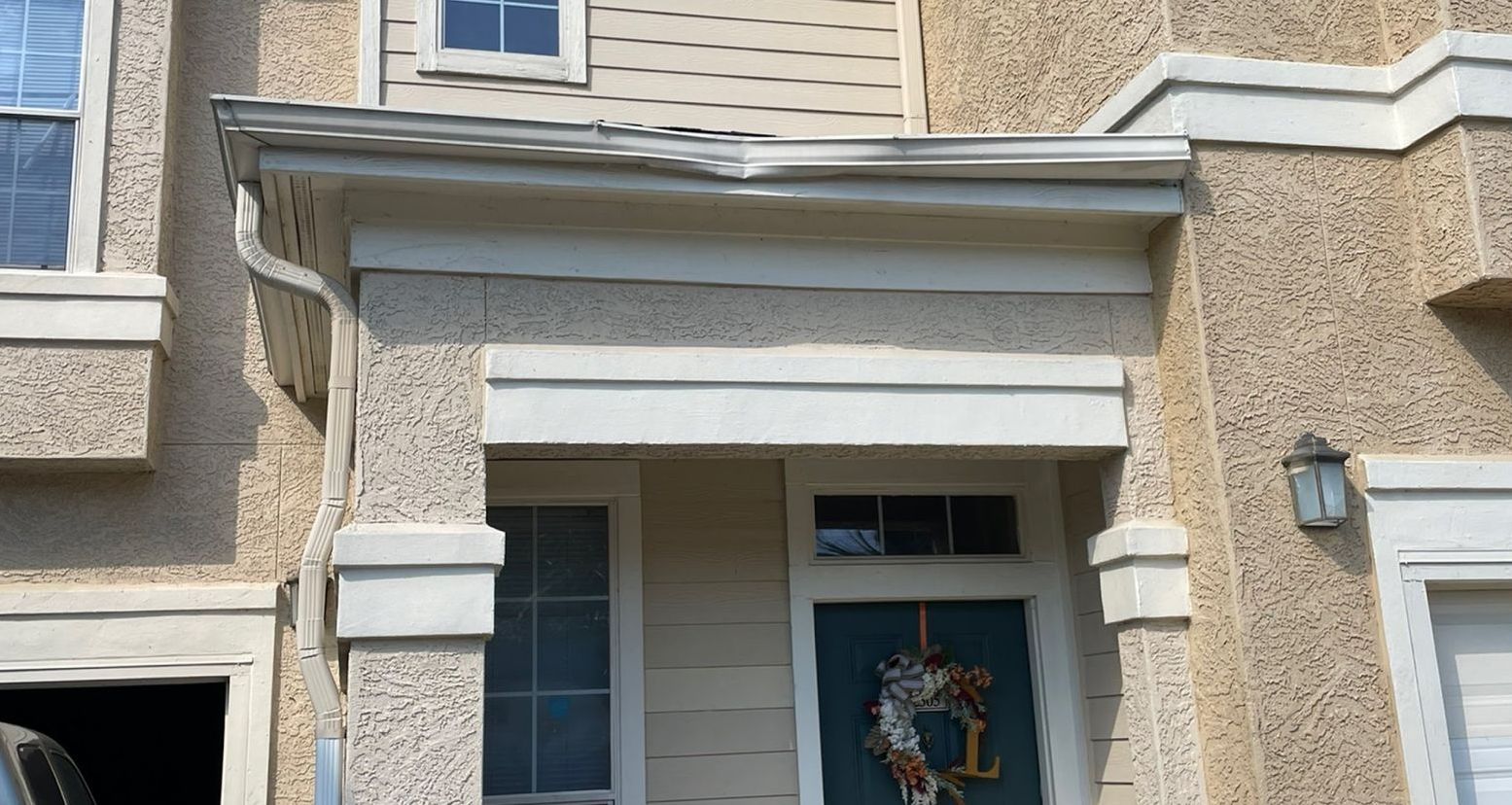 Tan stucco building with a white trim front entry, featuring a teal door adorned with a wreath.