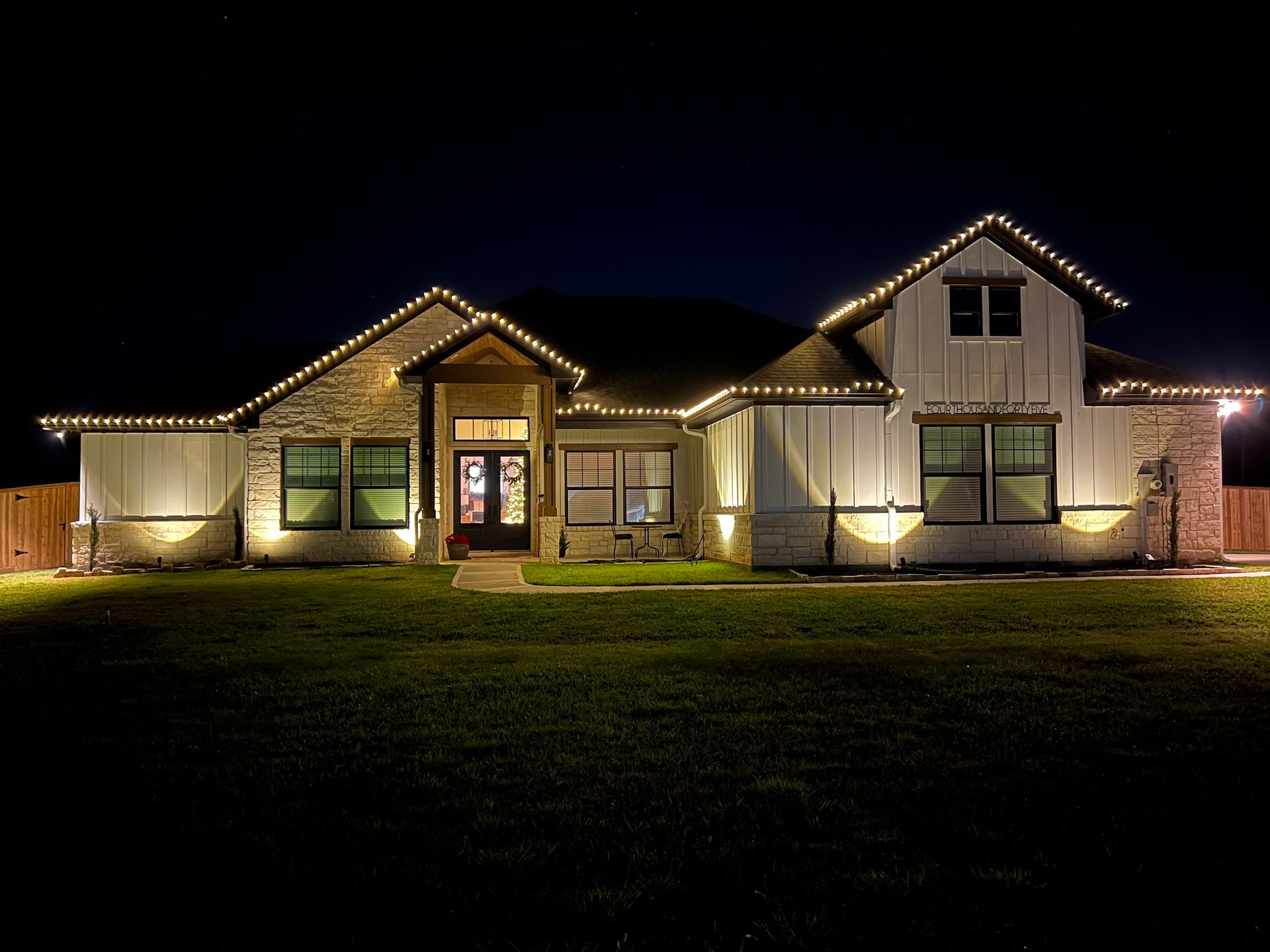 House exterior at night illuminated with warm white lights; festive holiday decorations.