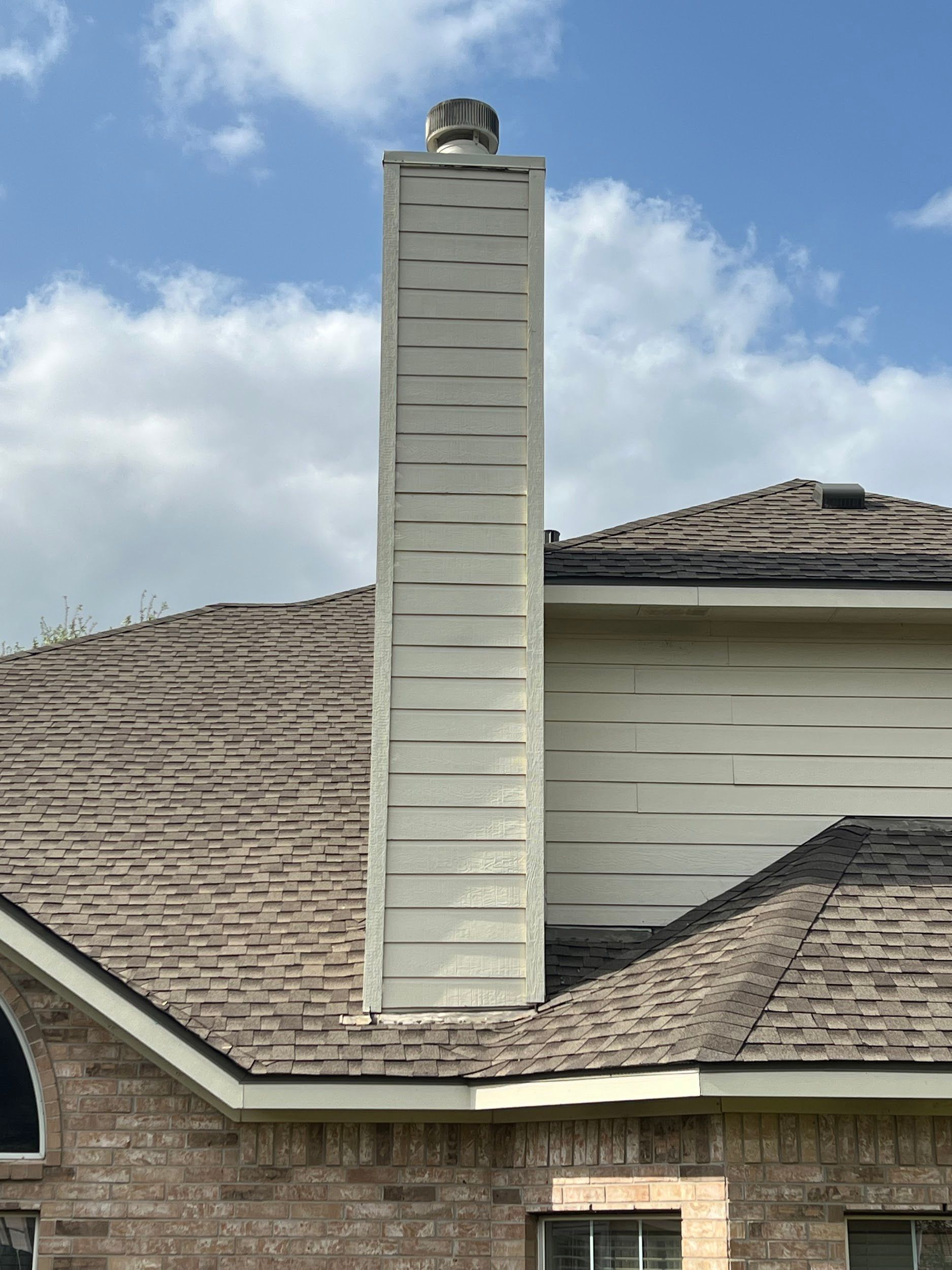 A tall, white chimney rises from a brown shingled roof against a cloudy blue sky.
