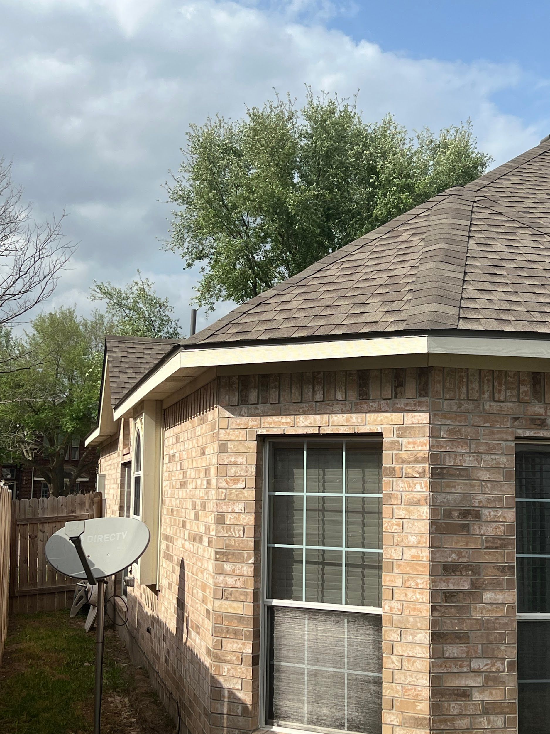 Brick house exterior with a brown shingled roof and window. A satellite dish is visible. Cloudy sky.