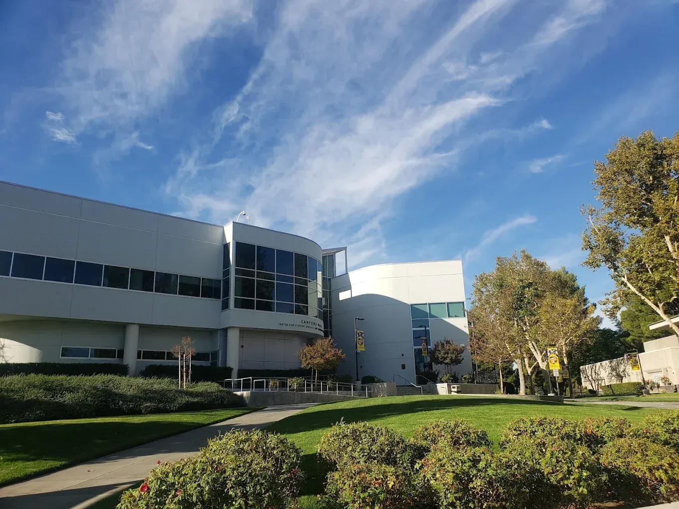 Modern building with glass windows, green lawn, trees, and a blue sky with clouds.