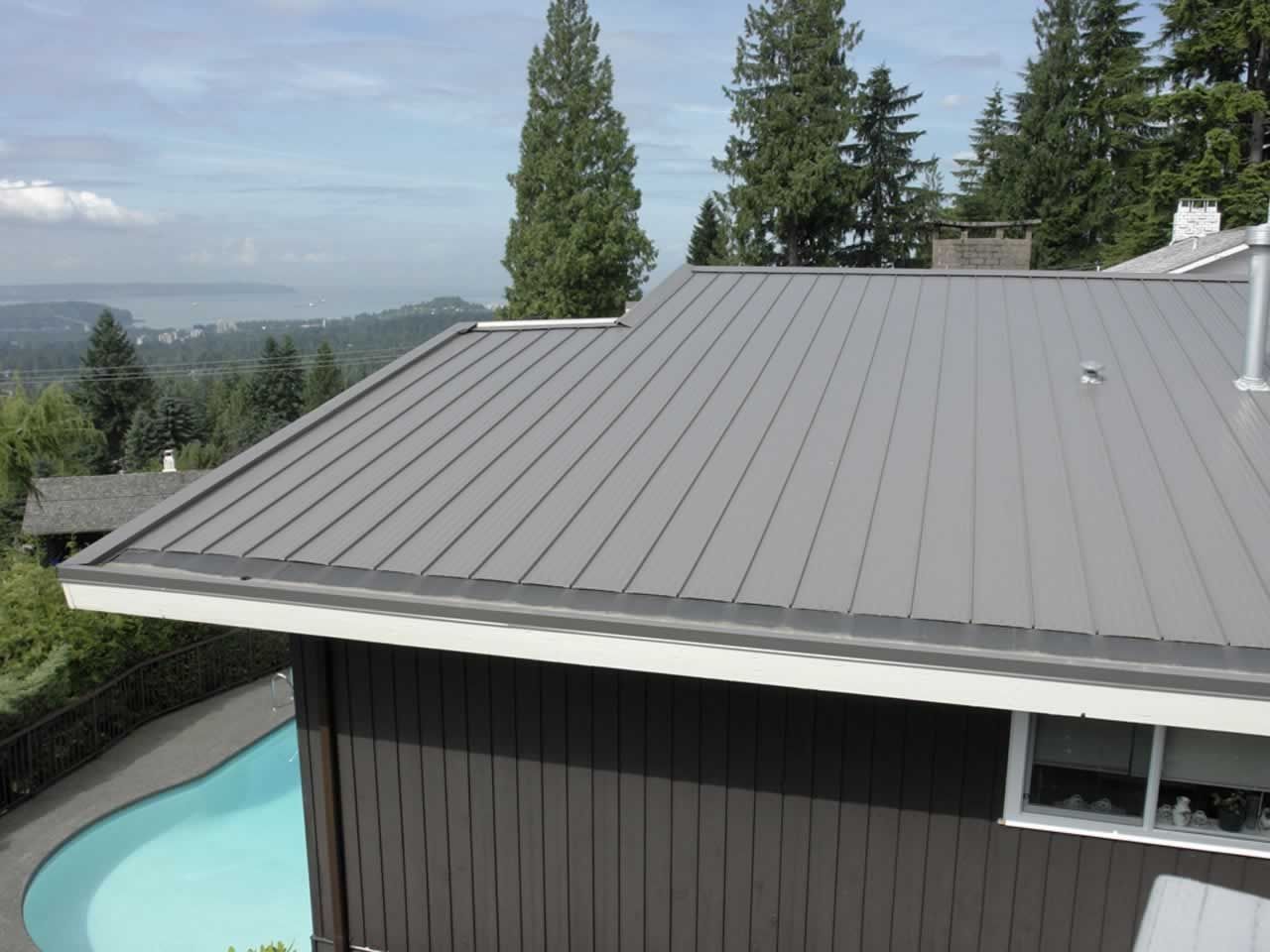 Gray metal roof on a house with a pool and trees in the background.