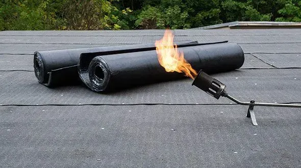 Torch-down roofing with a torch heating rolled roofing material on a flat roof.