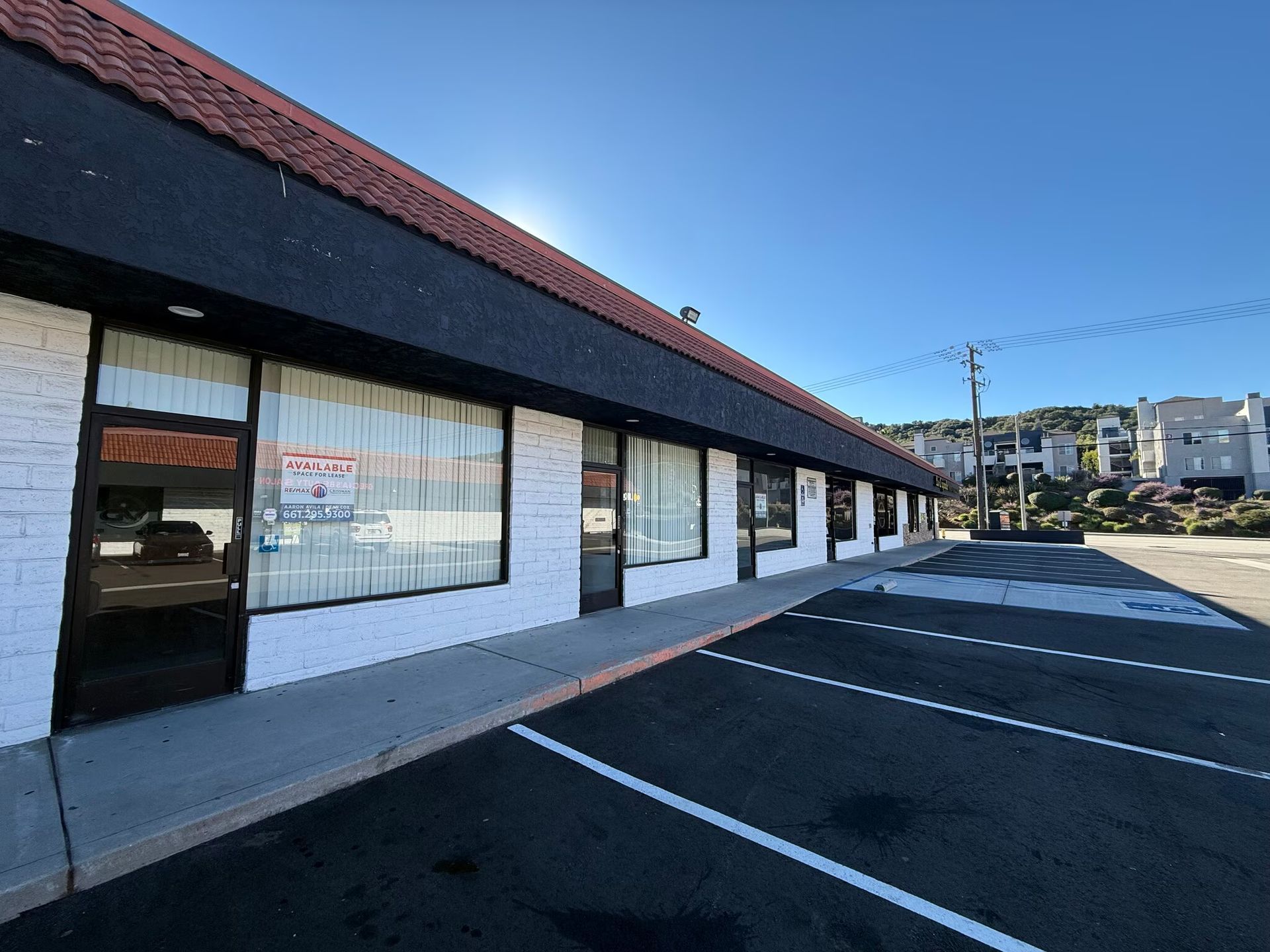 Exterior view of a commercial building with a black roof, white brick walls, and a parking lot.