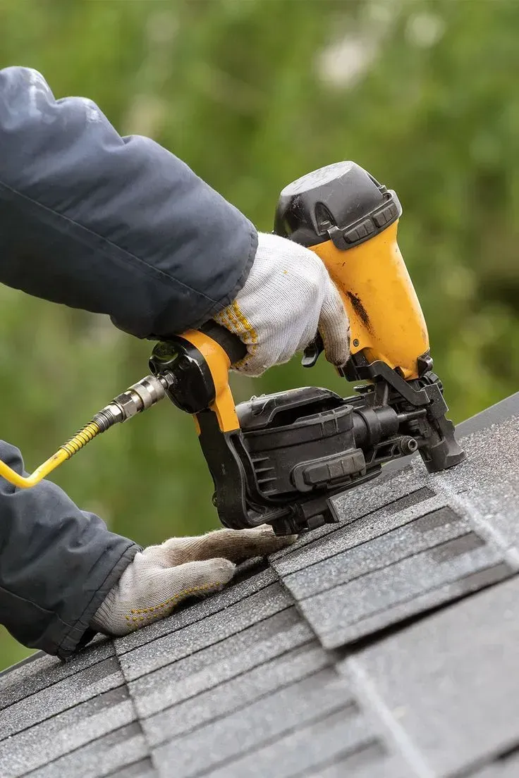 Person using a nail gun to install asphalt roof shingles.