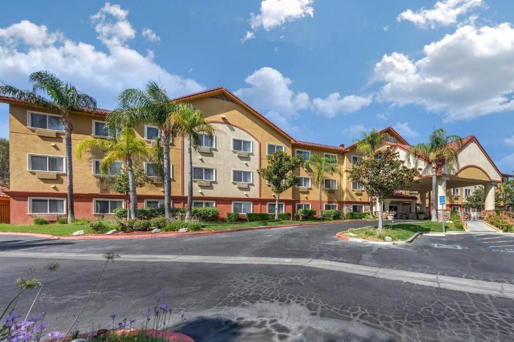 Hotel building with tan walls, red trim, palm trees, and blue sky.