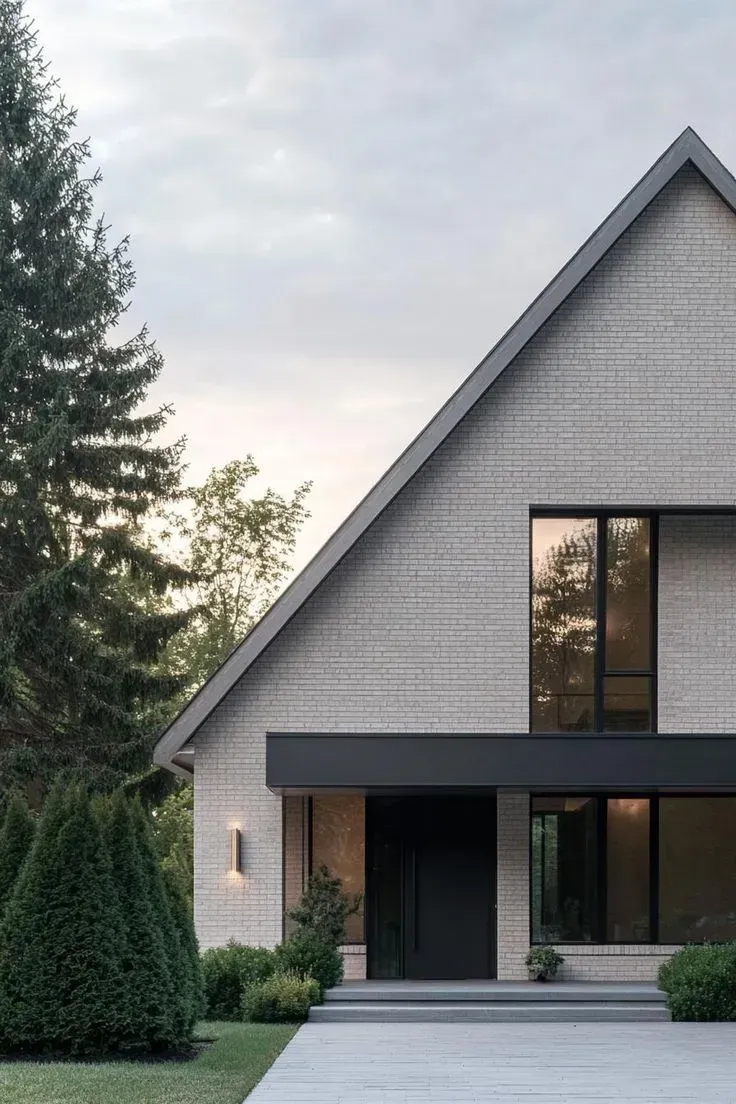 Modern house with gray brick facade, dark door, black trim, and large windows.
