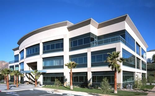 Three-story beige office building with large windows and palm trees under a blue sky.