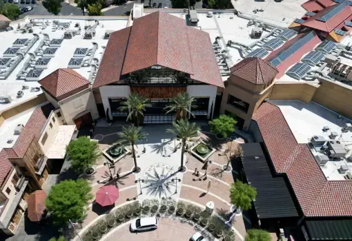 Aerial view of a shopping center courtyard with palm trees, walkways, and a large building with a terracotta roof.