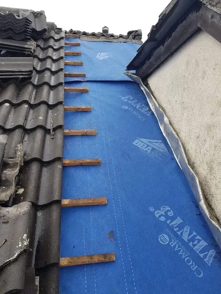 Roofing underlayment installed on a section of roof, with tiles on the left and exposed underlayment near a wall.