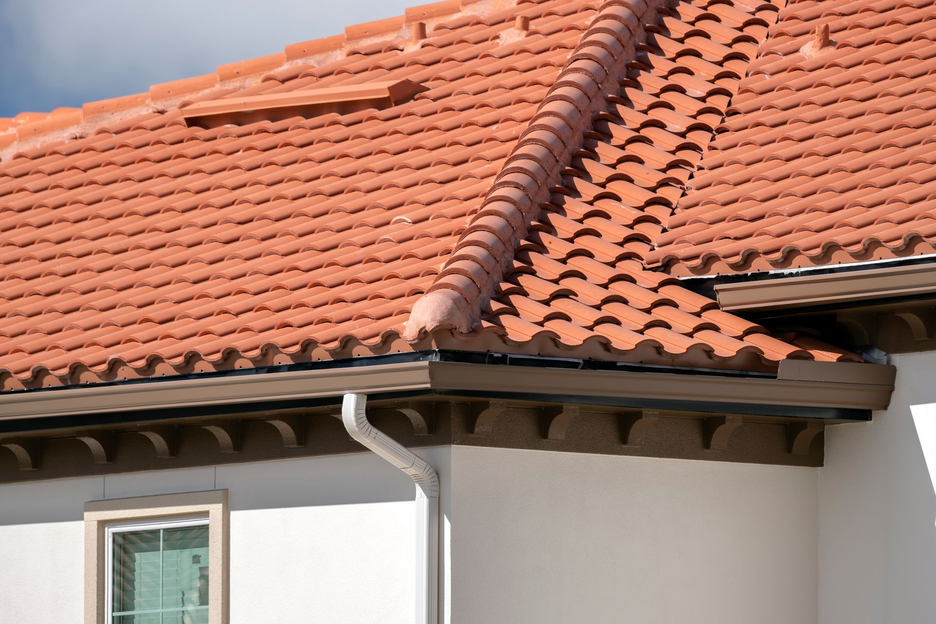Red tile roof with a white wall and a white downspout.